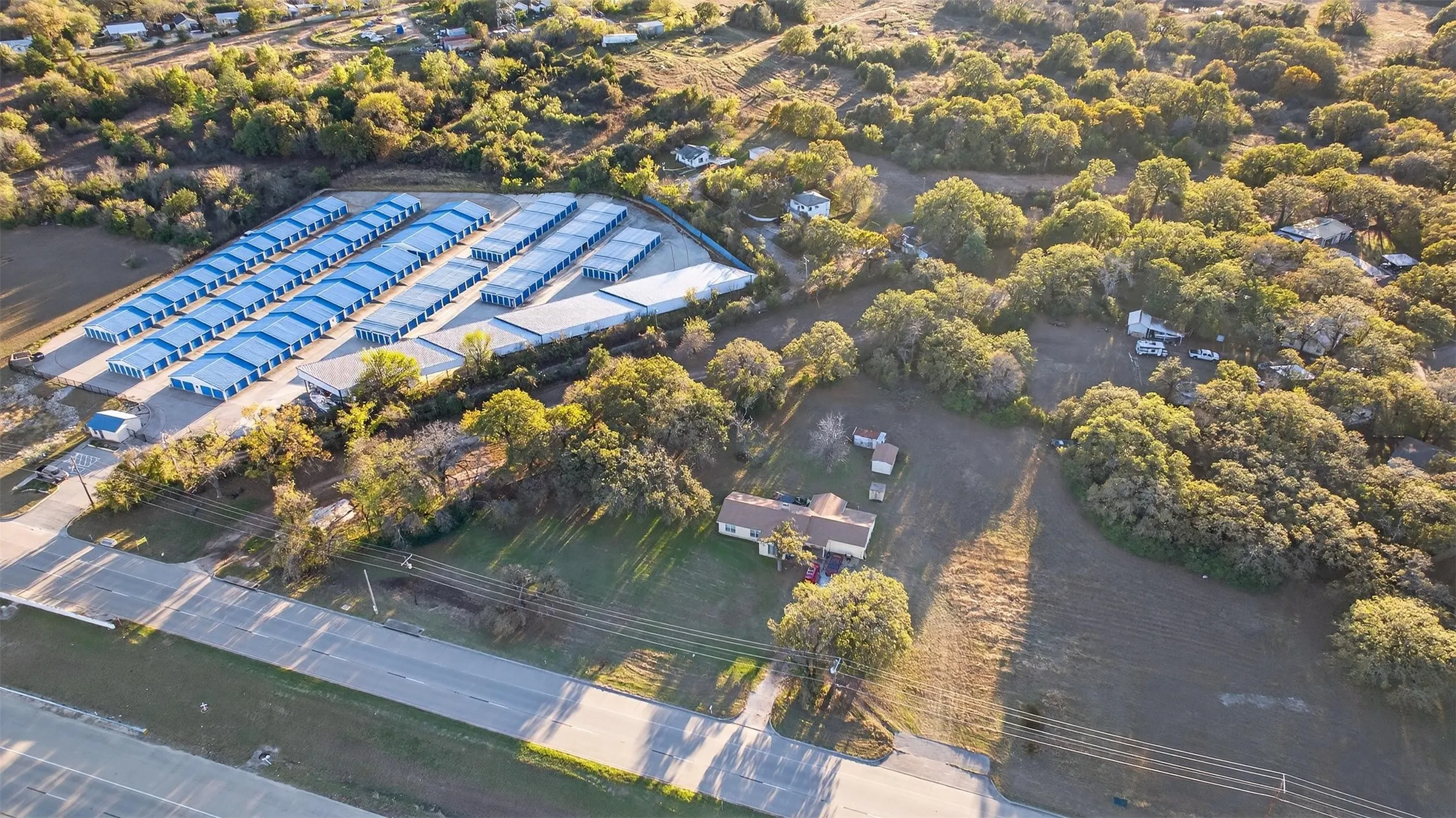 Aerial perspective showcasing a large-scale storage facility with multiple rows of units, a prominent roadway, and surrounding natural foliage