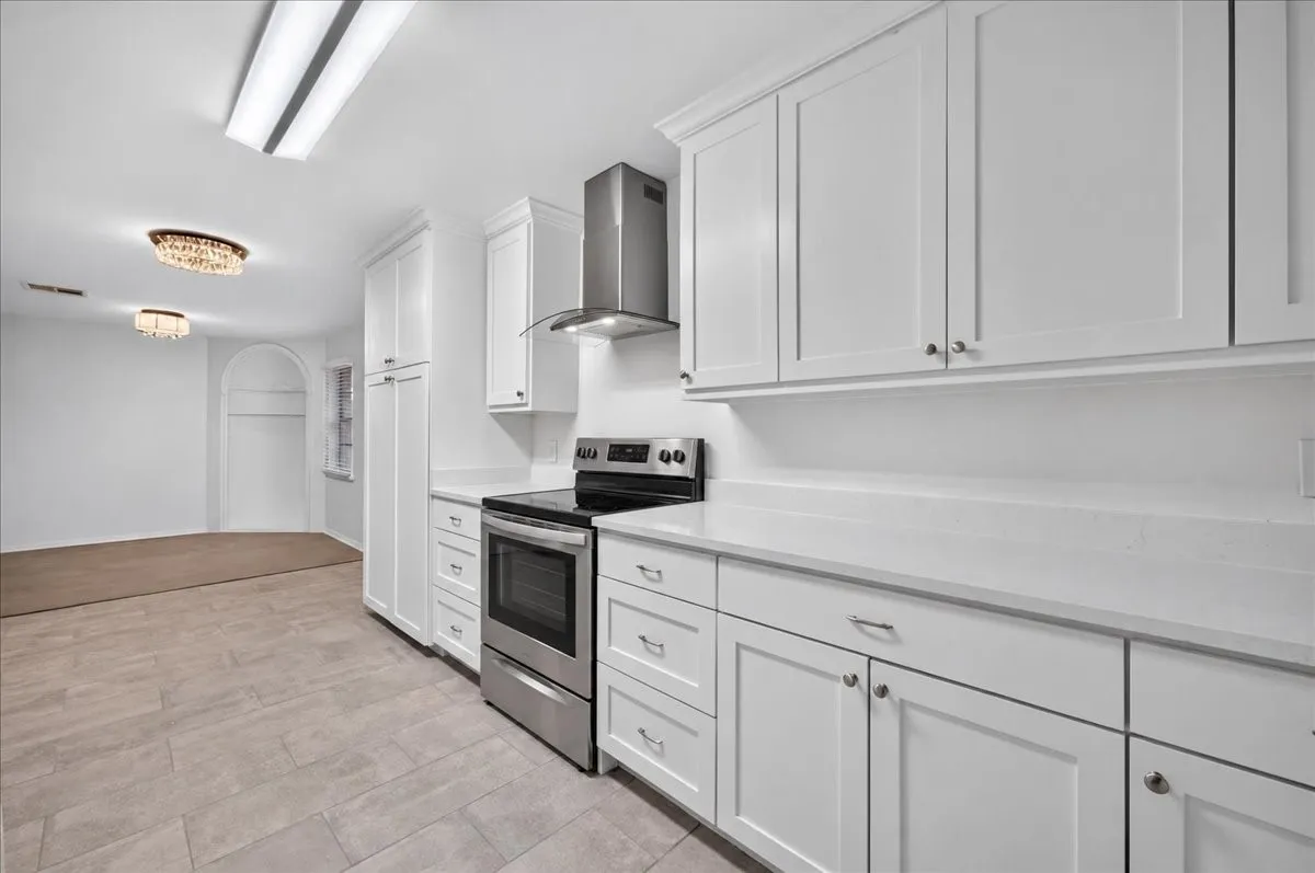 White shaker cabinetry with modern hardware, stainless steel range with overhead vent, light-toned countertops, and tile flooring