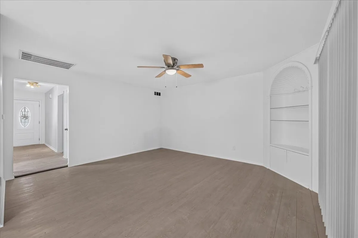 Wood-finish flooring, built-in shelving with arched detail, ceiling fan with light fixture, and white wall finishes