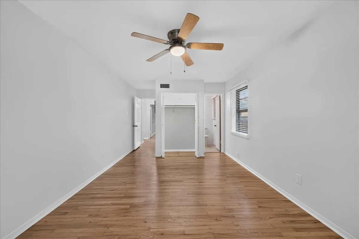 Wood-finish flooring, ceiling fan with integrated lighting, window with blinds, and white interior doors
