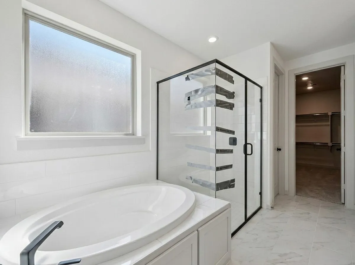 Oval soaking tub with matte black faucet, enclosed shower with black-framed glass, white subway tile accents, large frosted window, and marble-look floor tiling