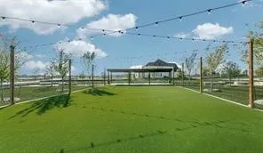 Expansive outdoor space featuring artificial turf, string lighting, and a distant covered pergola