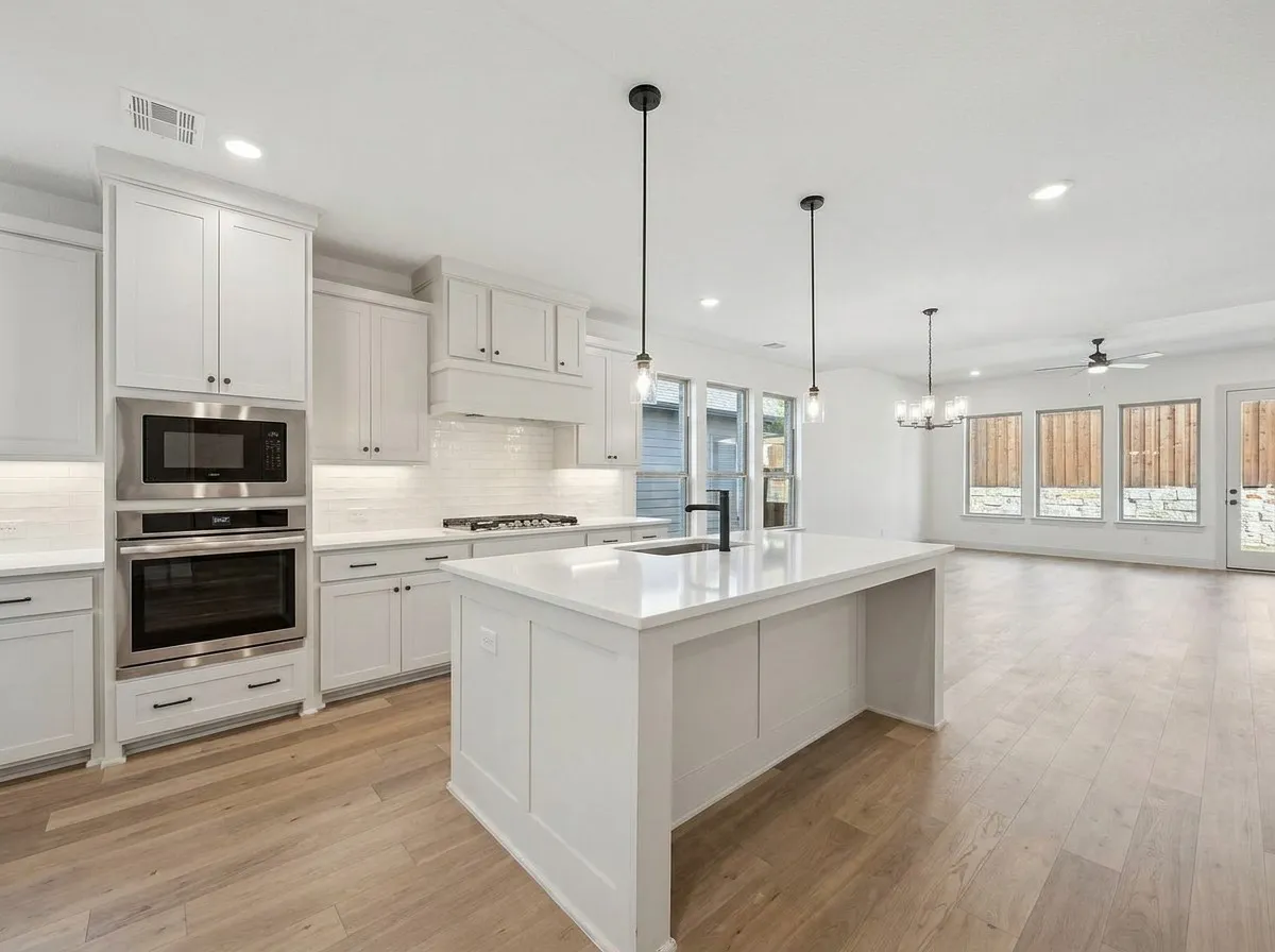 Open-concept living space with wood-finish flooring, white cabinetry, a kitchen island with a sink, and stainless steel appliances