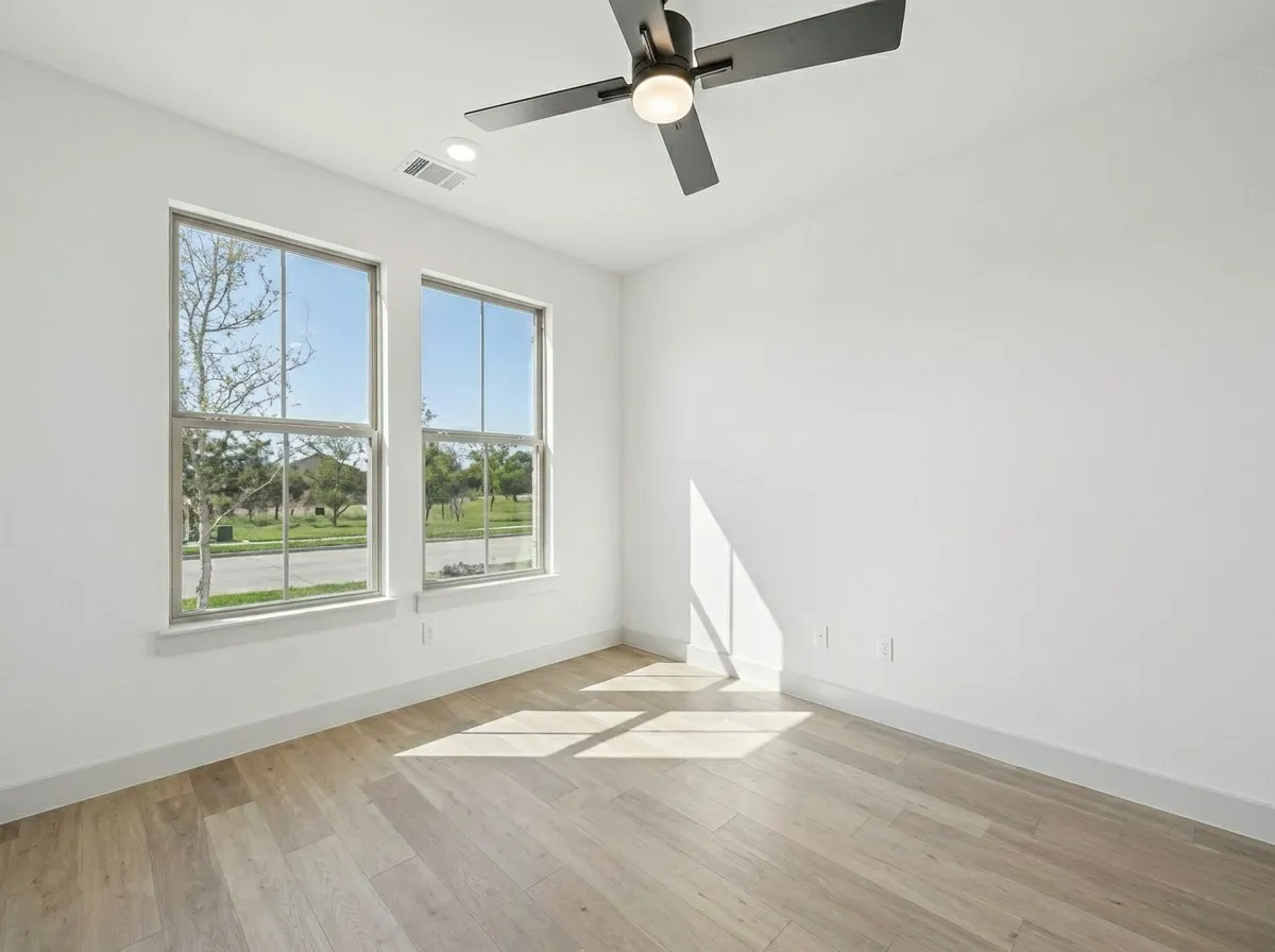 Light wood-finish flooring with white baseboards, dual windows, recessed lighting, and a ceiling fan with integrated light