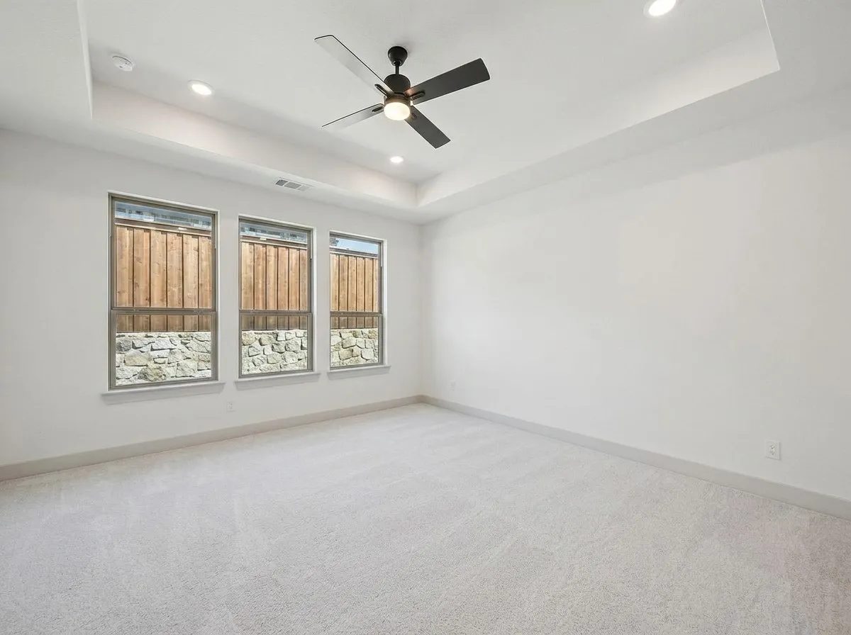 Recessed lighting, three windows, a ceiling fan, tray ceiling, and light-colored carpeting
