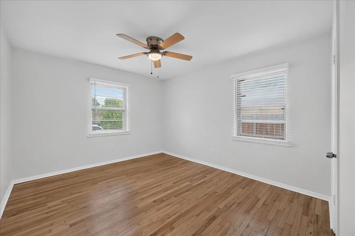 Hardwood flooring, painted walls, two windows with blinds, and a ceiling fan with integrated lighting