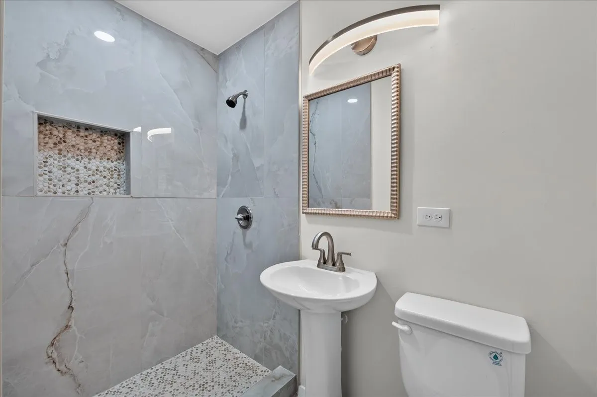 Pedestal sink with a brushed nickel faucet, framed mirror, and modern arched vanity light