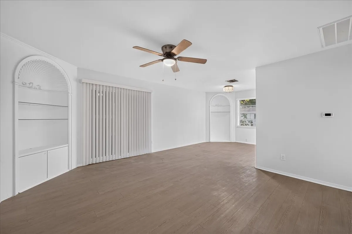 Wood-finish flooring, built-in arched shelving, ceiling fan, white vertical blinds, and recessed lighting