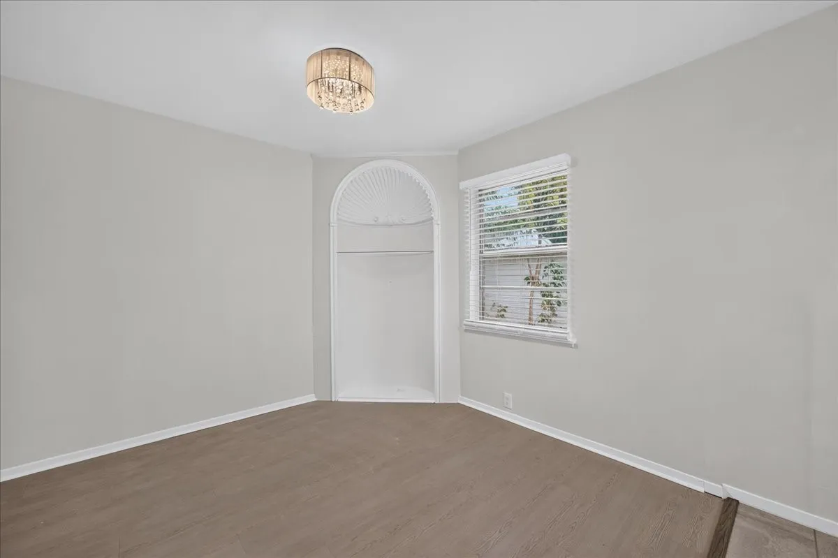 Wood-finish flooring, recessed built-in shelving, window with blinds, and a decorative flush-mount light fixture