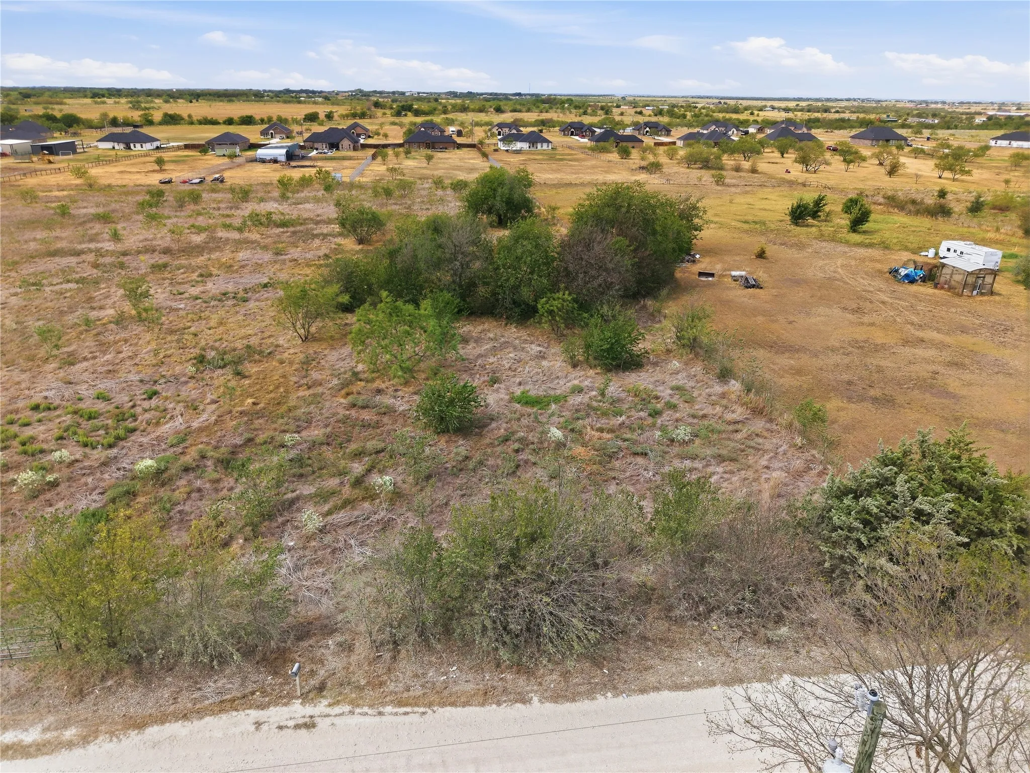 Expansive open land featuring natural vegetation and distant residential structures under a clear sky