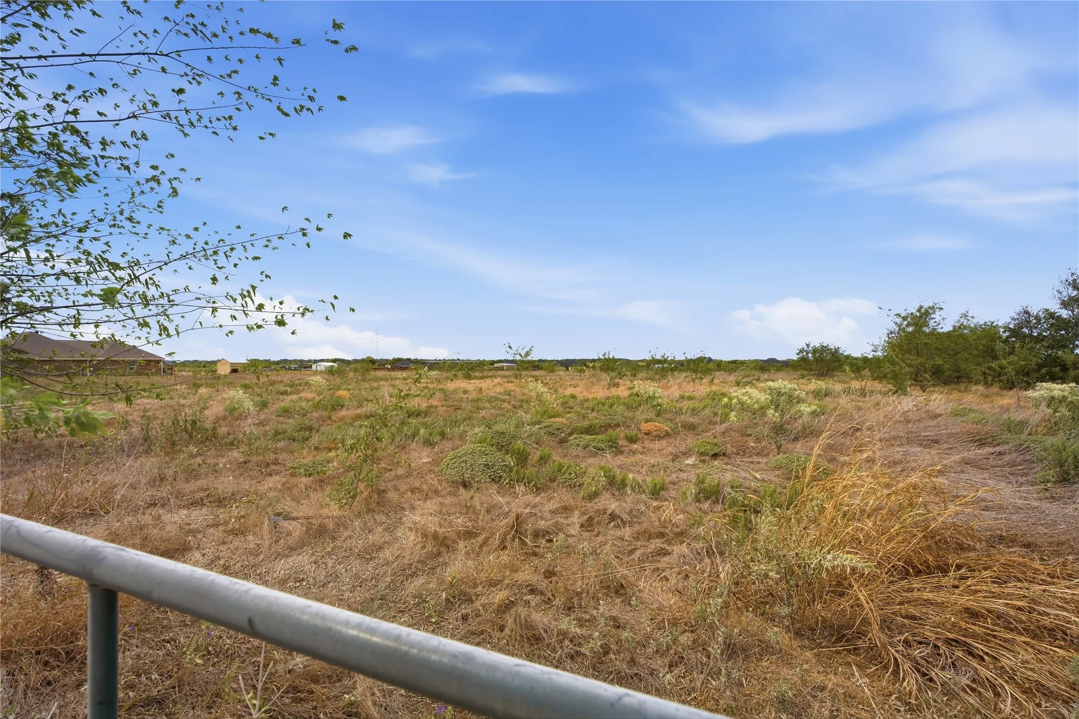 Expansive undeveloped land featuring natural vegetation and distant structures under a clear sky