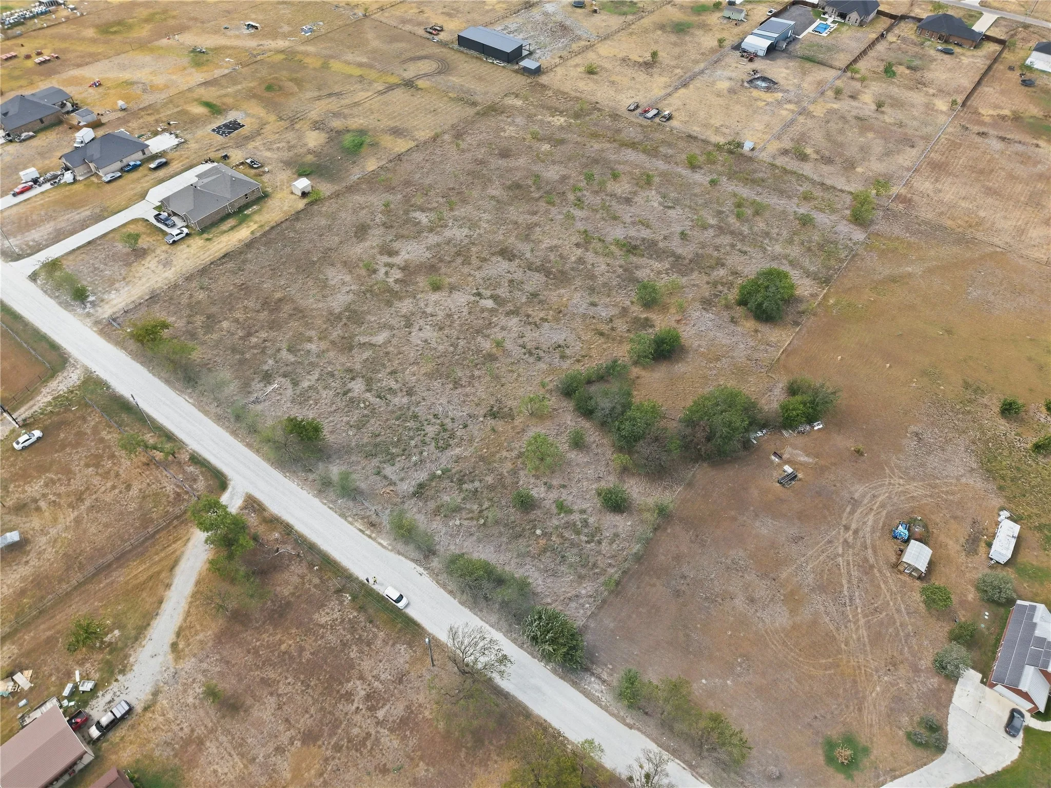 Expansive parcel featuring a paved road, scattered trees, and adjacent developed properties
