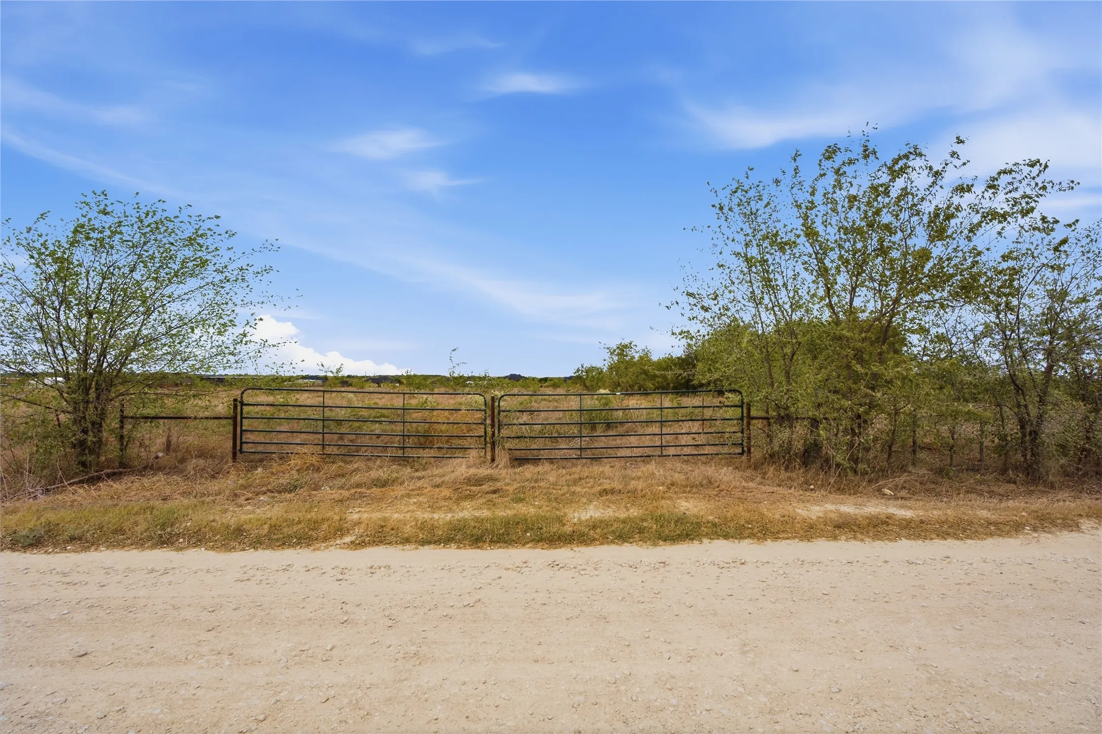 Expansive open land featuring an entry gate, natural vegetation, and a clear sky