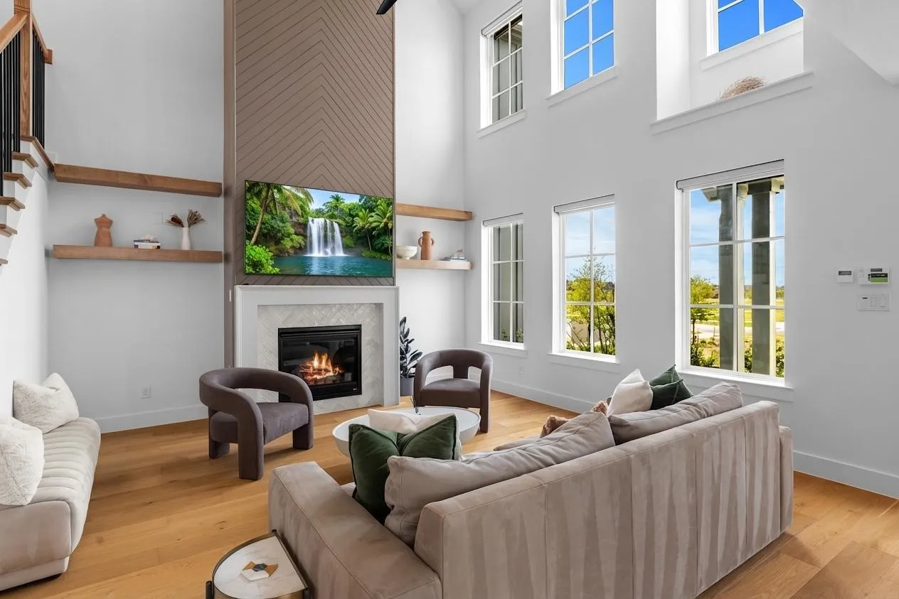 Spacious living area featuring a fireplace with a light-toned surround, wood-finish flooring, high ceilings, and multiple transom windows