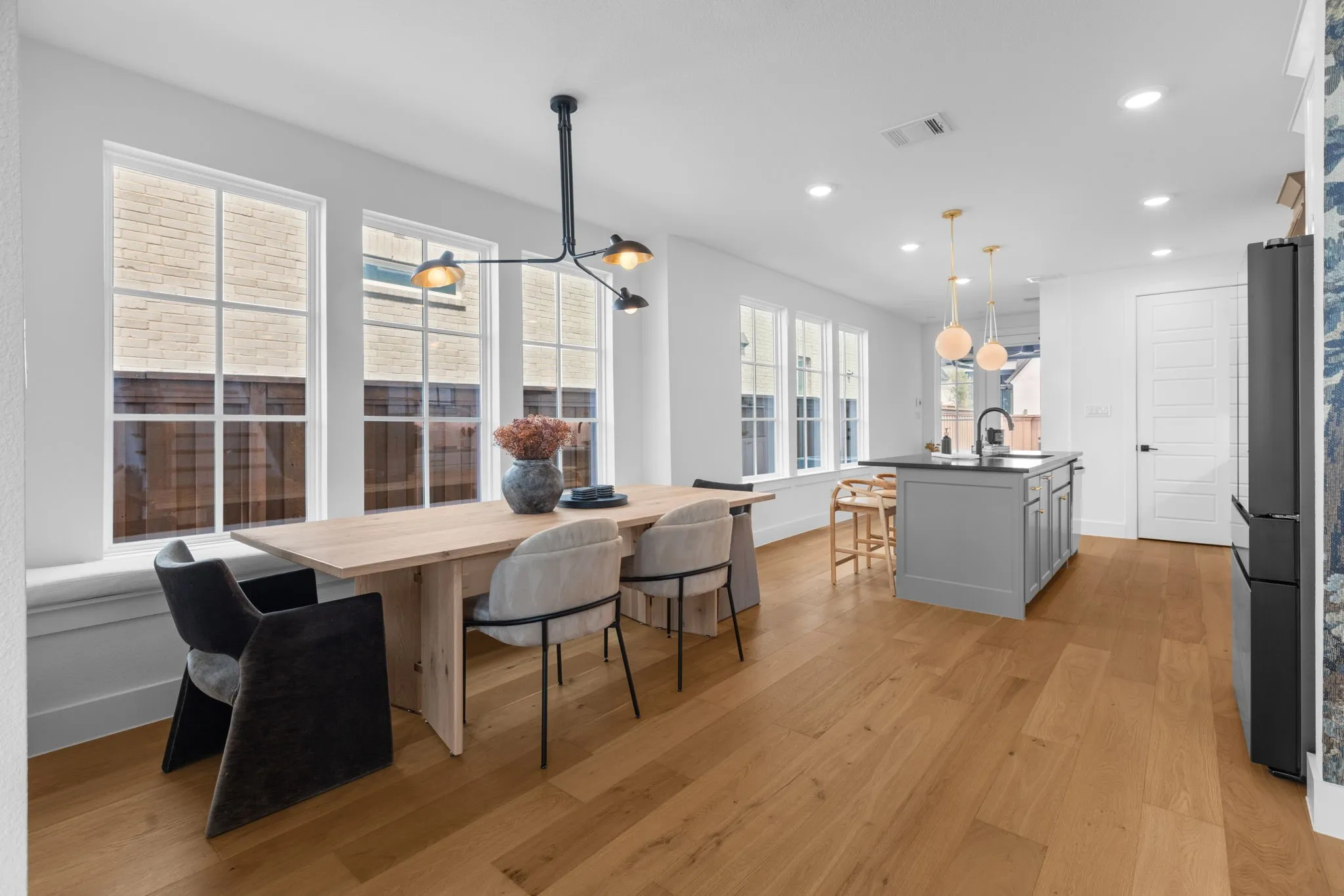 Wood-finish flooring, white walls, multiple large windows, kitchen island with dark countertop, and recessed lighting