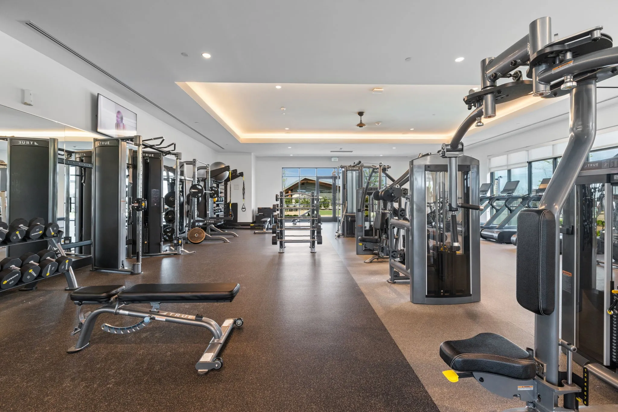 Fitness center featuring extensive exercise equipment, rubberized flooring, large windows, recessed lighting, and a tray ceiling