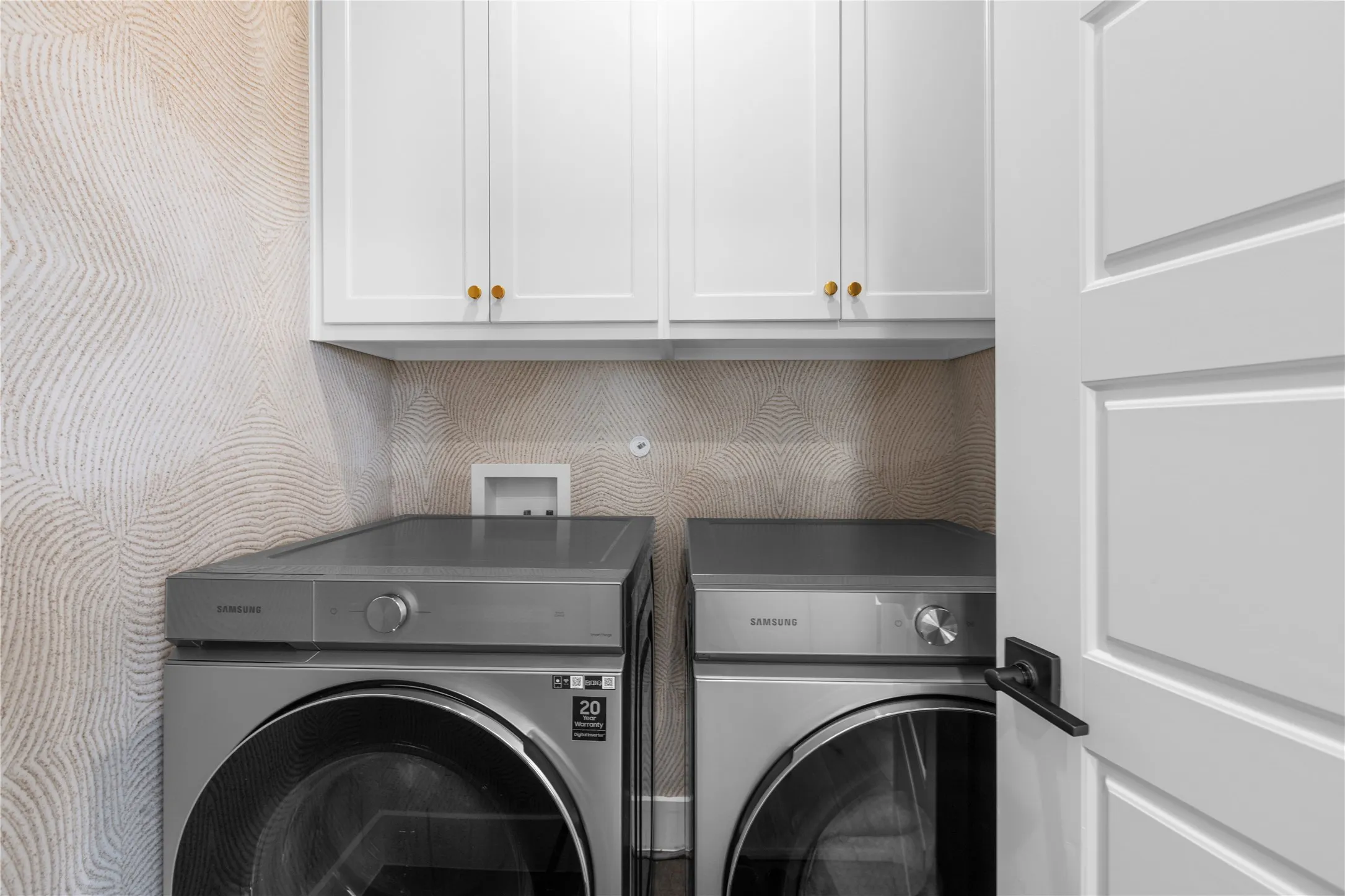 White shaker-style cabinetry with gold-tone hardware, textured wall covering, and a white interior door with matte black hardware