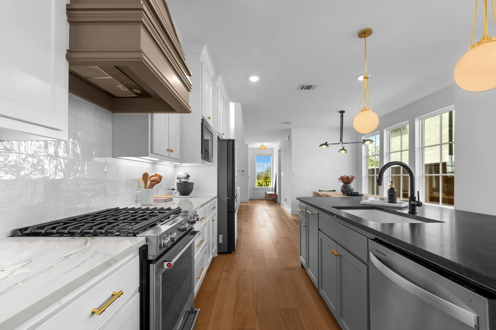 Gourmet kitchen featuring a built-in range, white shaker cabinetry, white tile backsplash, a dark-toned island with an undermount sink, and wood-finish flooring