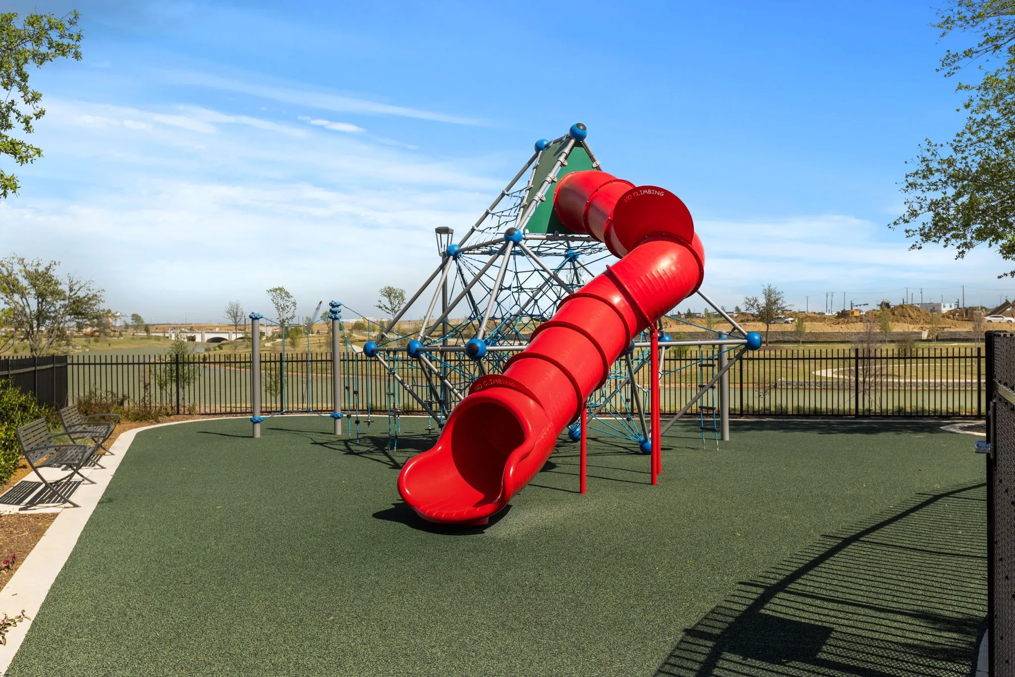 Recreational playground featuring a climbing structure, red slide, and a green soft-fall surface