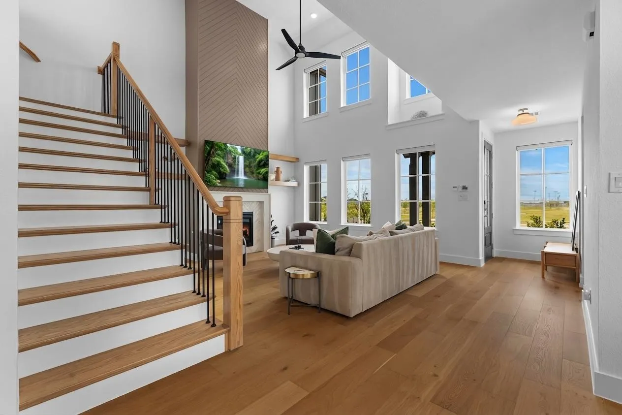 Vaulted ceiling with a contemporary ceiling fan, wood-finish flooring, a fireplace with a mantel, and a staircase with wood treads and metal balusters