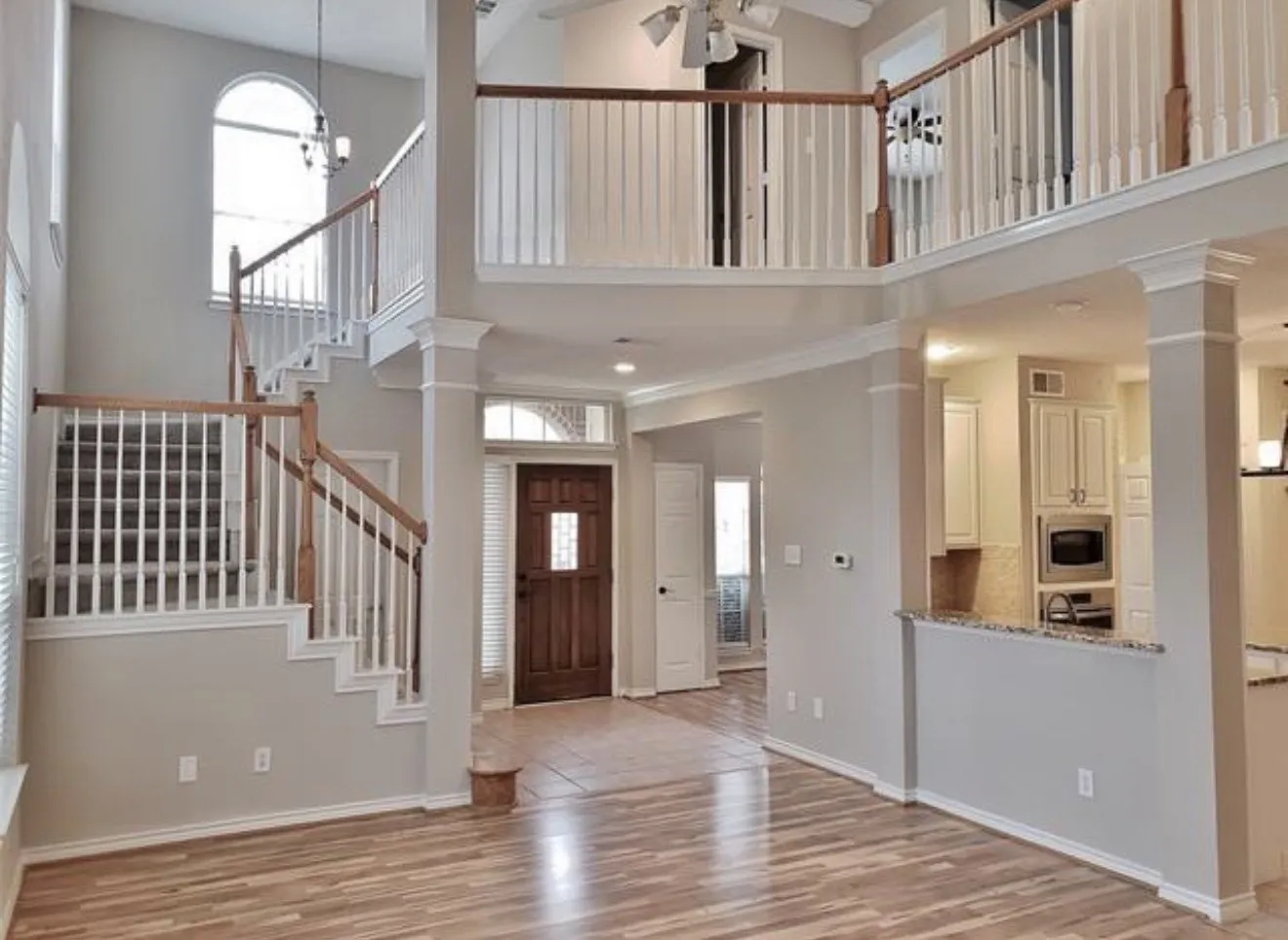 Two-story foyer with wood-finish flooring, grand staircase with wood railing, and an arched transom window