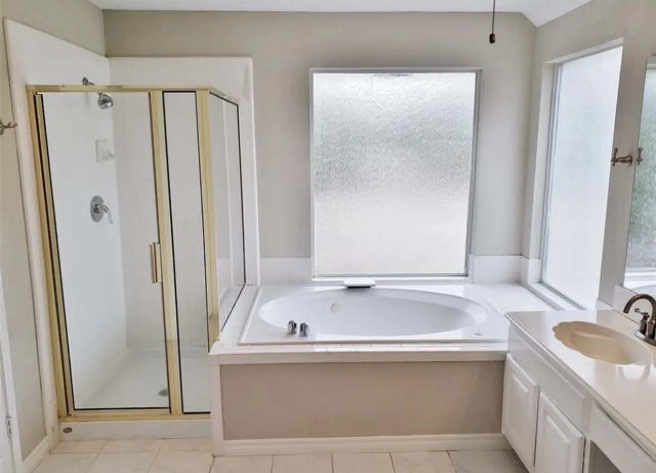 White tile flooring with an embedded tub, an enclosed shower with gold-tone framing, and a vanity with an integrated sink