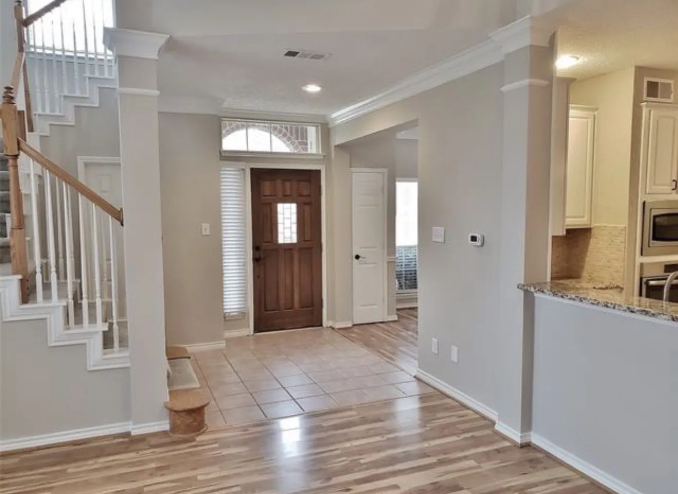 Wood-finish flooring, staircase with wood handrail, tiled entry, wood-paneled door with glass insert, and granite countertops