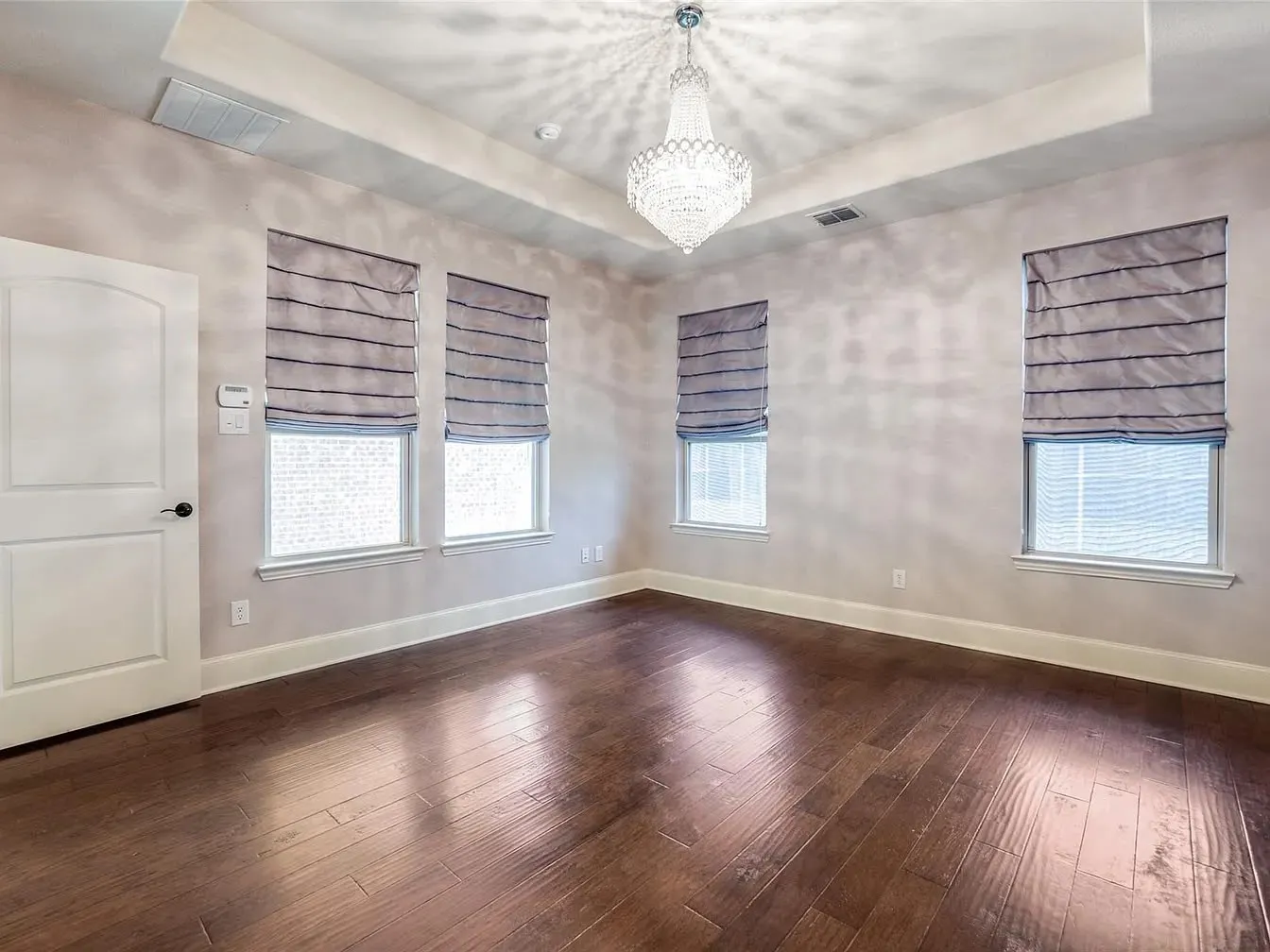 Hardwood-style flooring, tray ceiling, crystal chandelier, multiple windows with blinds, and a paneled door