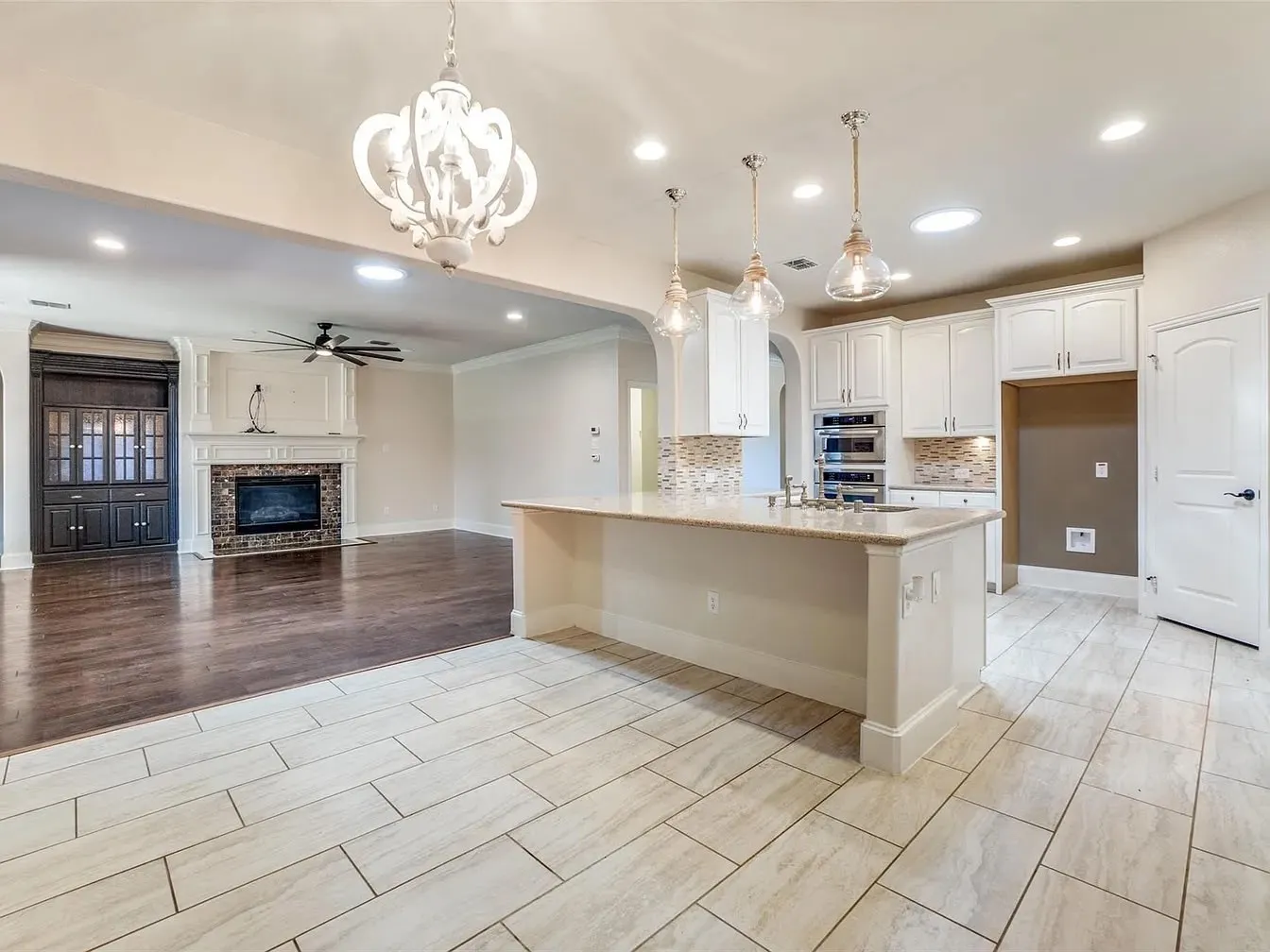 White shaker cabinetry, light-toned tile flooring, recessed lighting, and a prominent fireplace with a detailed mantel