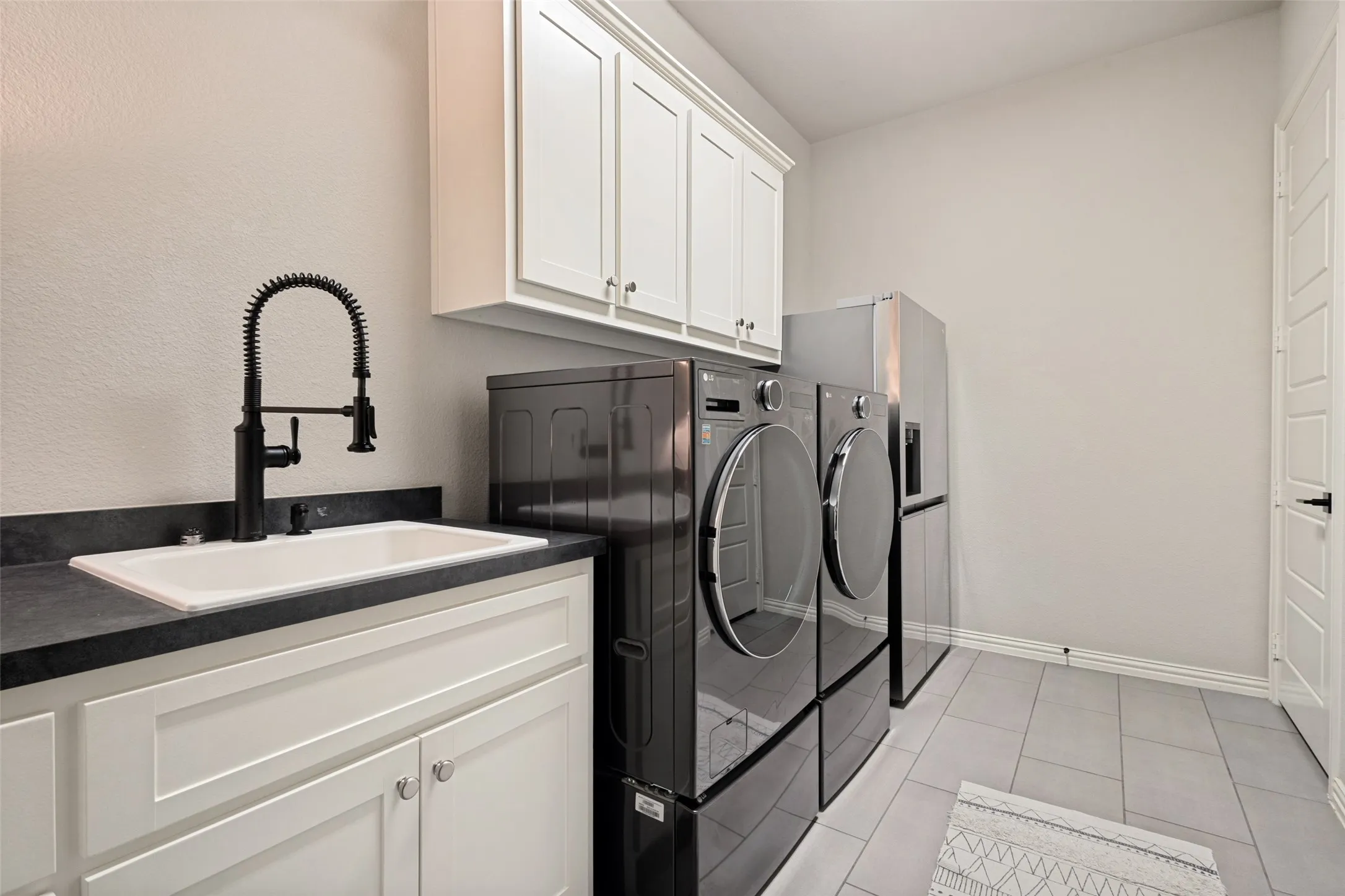 Utility room featuring light-toned walls, white cabinetry with silver hardware, a white soaking sink, with a black gooseneck faucet and room for a freezer or second refrigerator