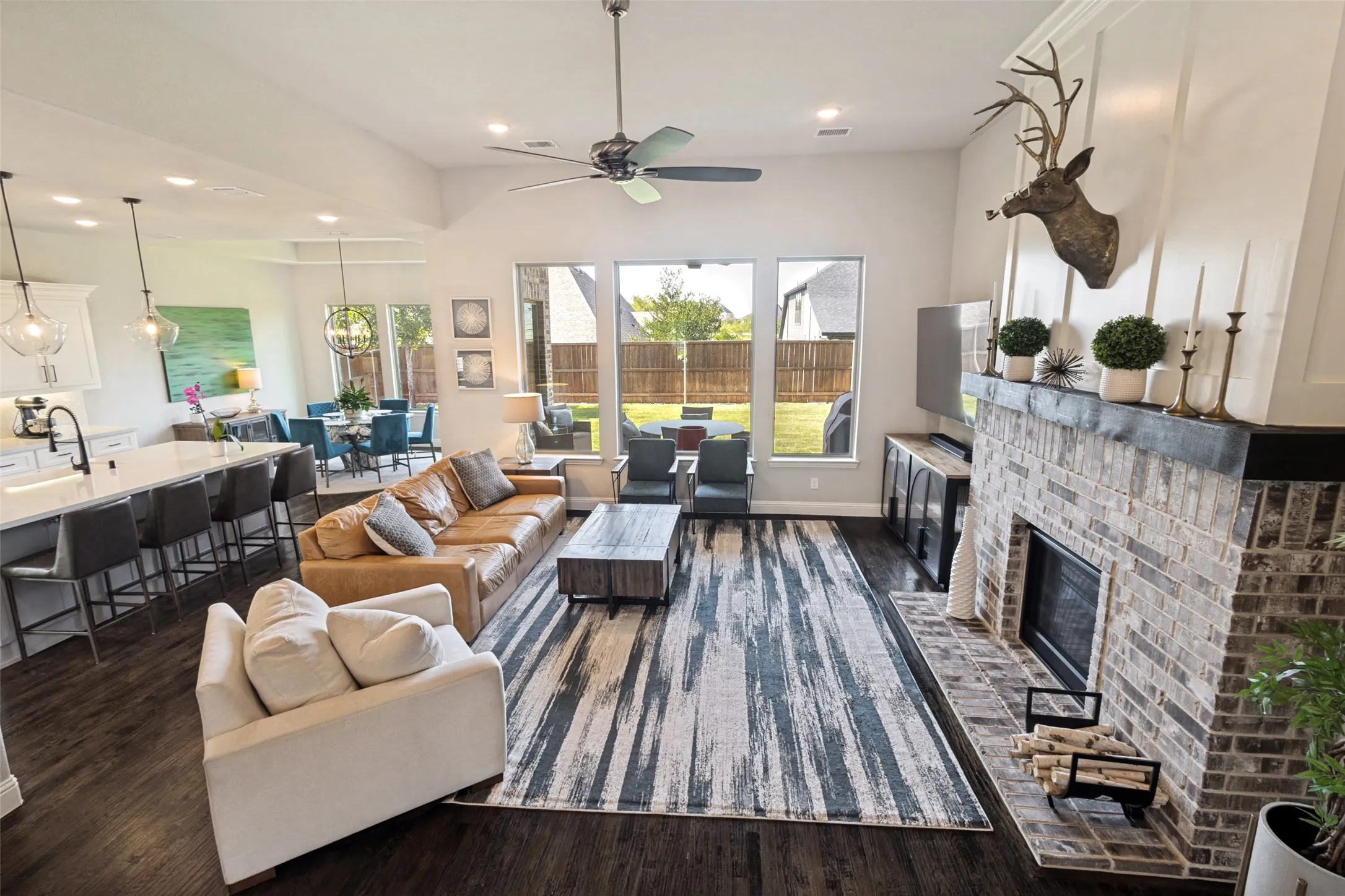Expansive open-concept living area with high ceilings, dark wood flooring, and a brick fireplace featuring a wood mantle