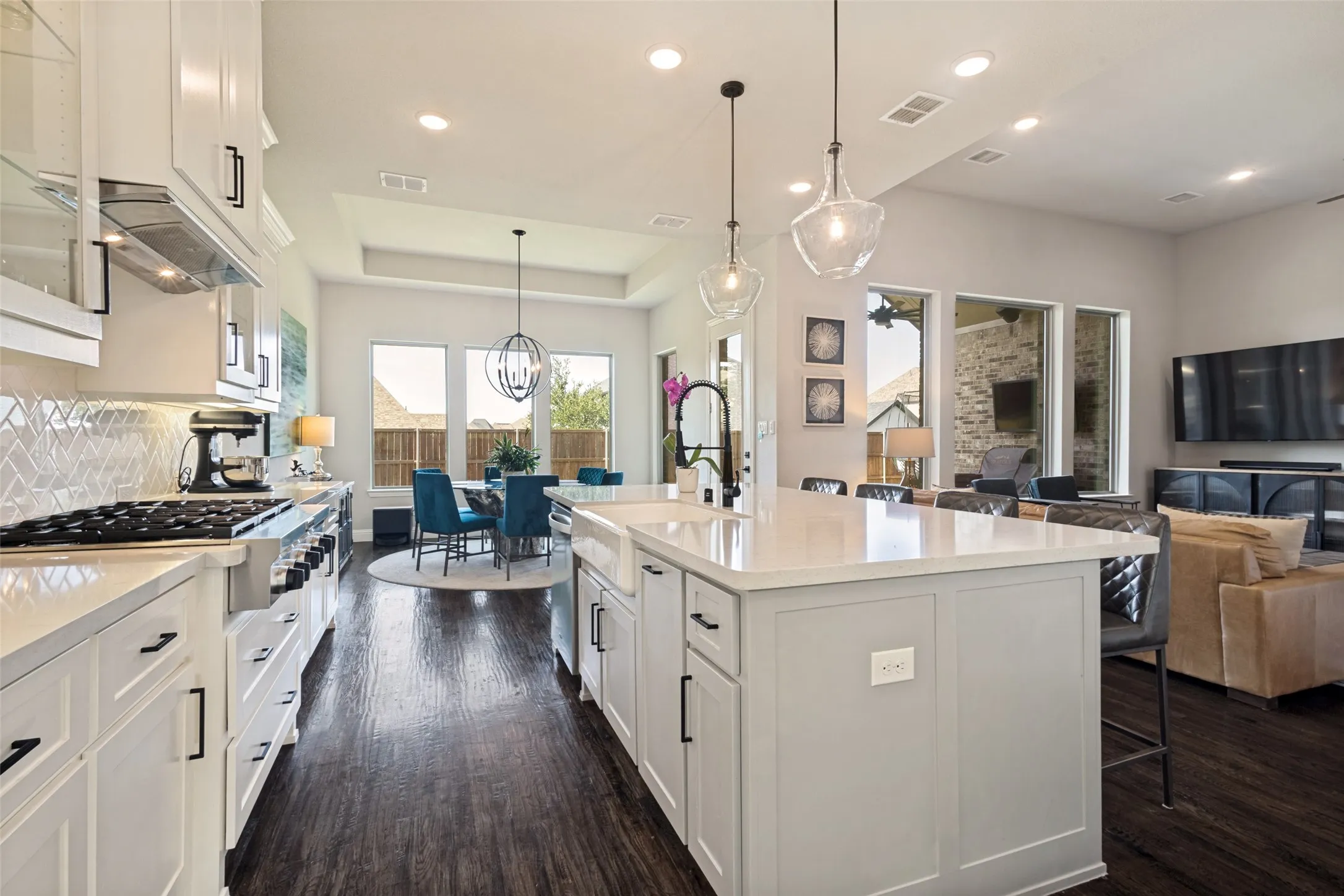 Gourmet kitchen featuring a commercial-styler gas range, white cabinetry, a large island with a farmhouse sink, and elegant pendant lighting, all opening to the breakfast room and family room