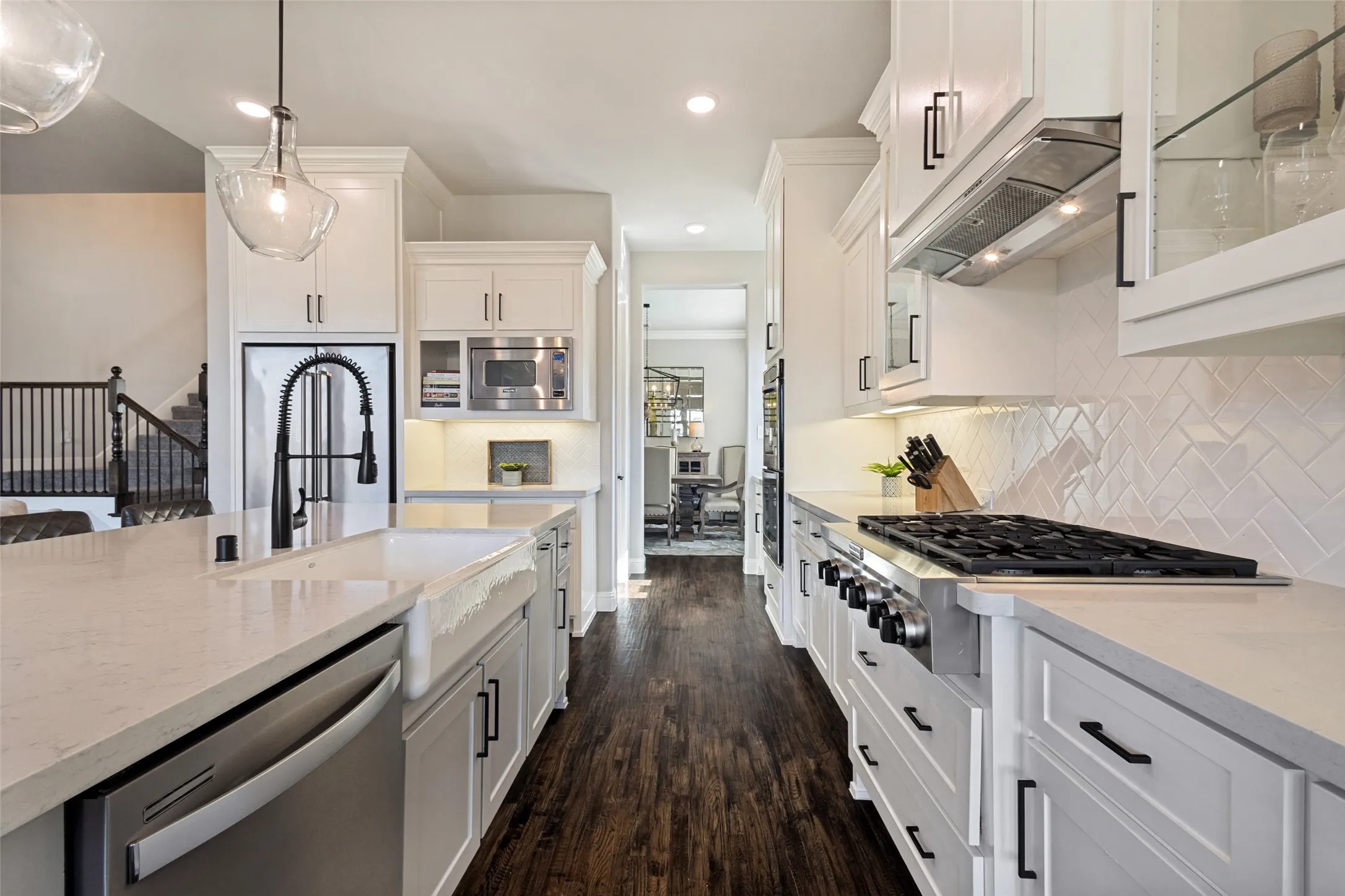 White shaker cabinetry with dark hardware, stainless steel appliances, solid surface countertops, herringbone tile backsplash, and dark wood-finish flooring