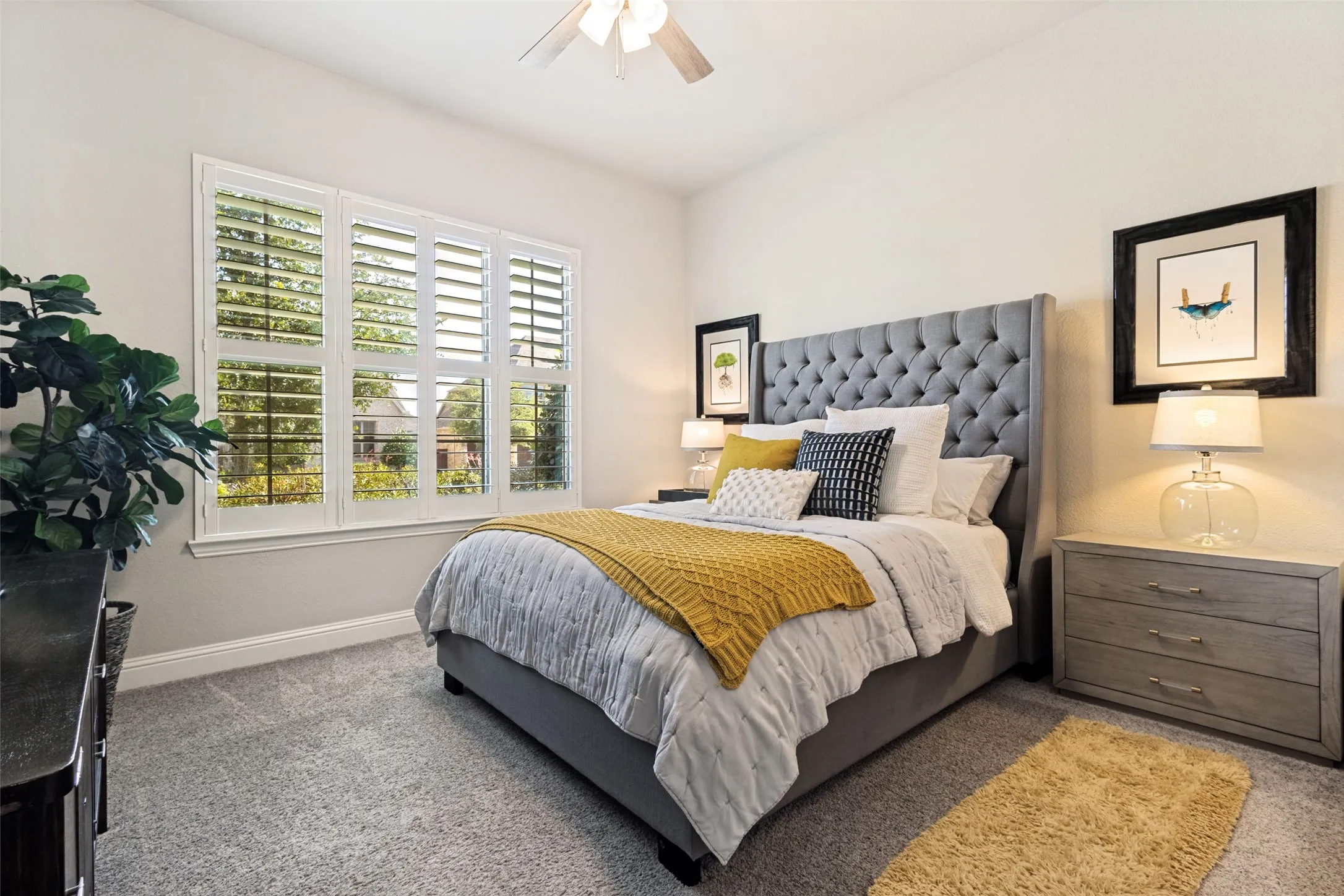 Downstairs guest bedroom featuring it's own private bathroom and walk-in closet, a ceiling fan, large window with white plantation shutters, gray textured carpeting, and light gray wall paint