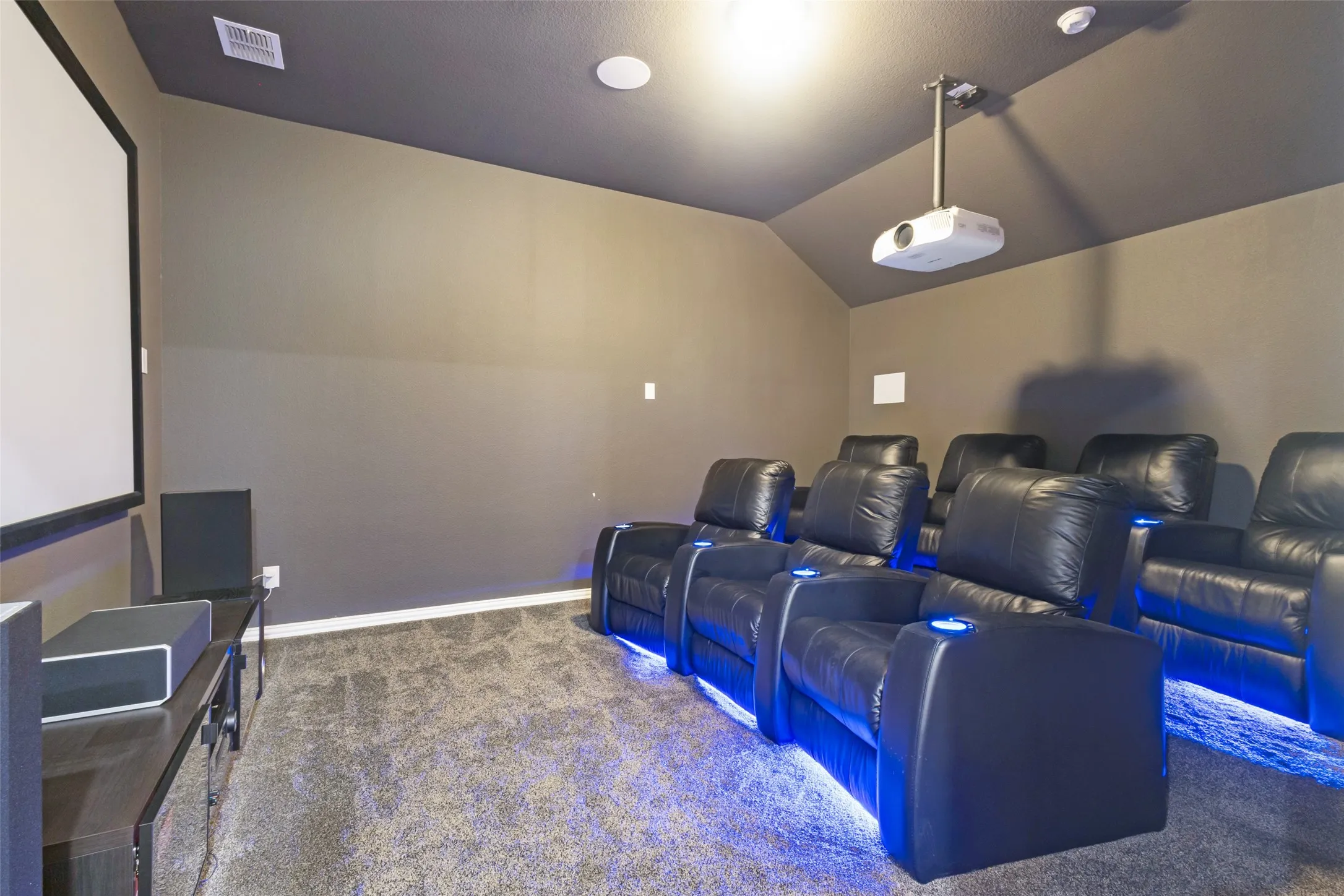 Dedicated media room featuring a large projection screen and ceiling-mounted projector. Speakers are set up in a Dolby Atmos setup