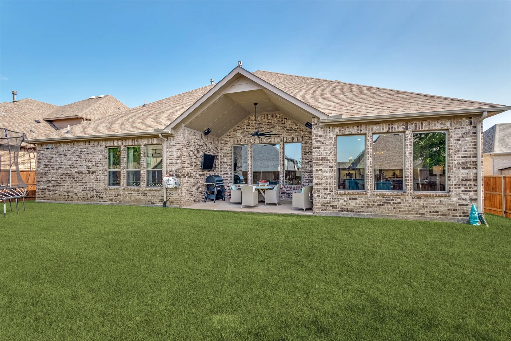 Spacious backyard featuring a brick exterior, covered patio, large picture windows, and a generous lawn area
