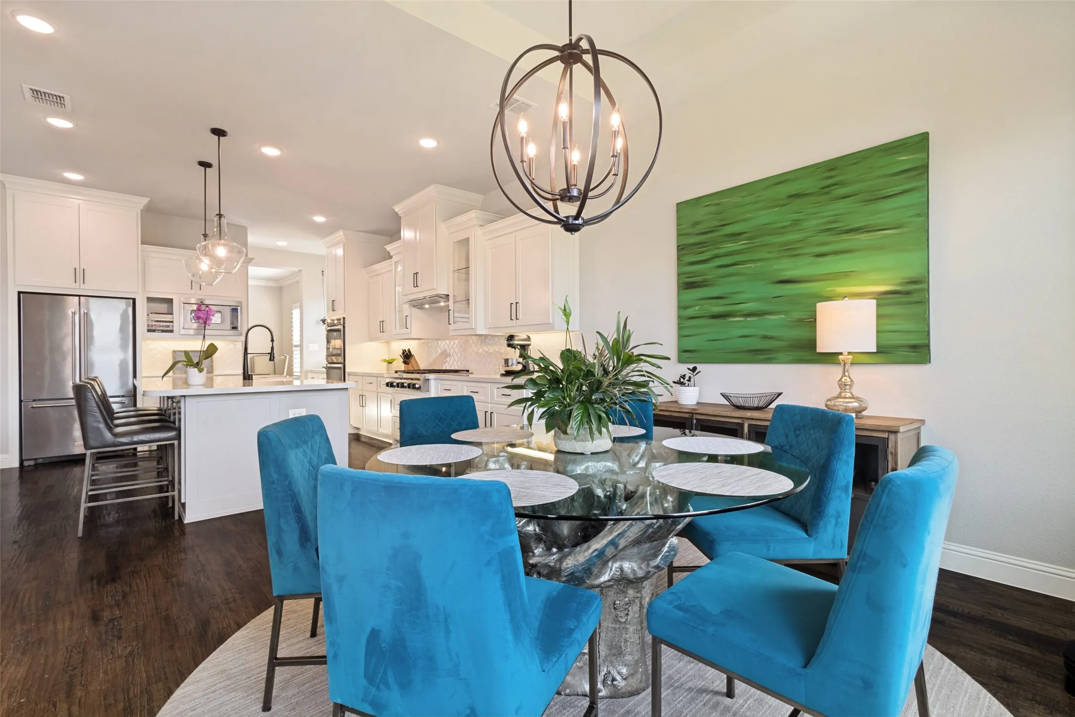 Open-concept breakfast area featuring solid hardwood flooring, a contemporary spherical chandelier, and a spacious kitchen with white cabinetry and stainless-steel appliances