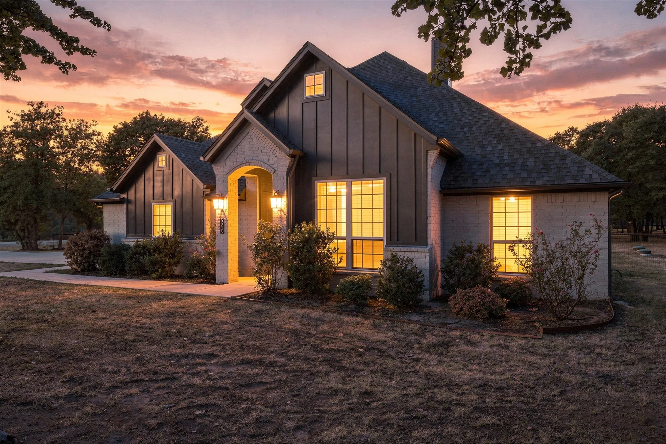 Board and batten siding, brick exterior, arched entry, covered porch, and exterior lighting