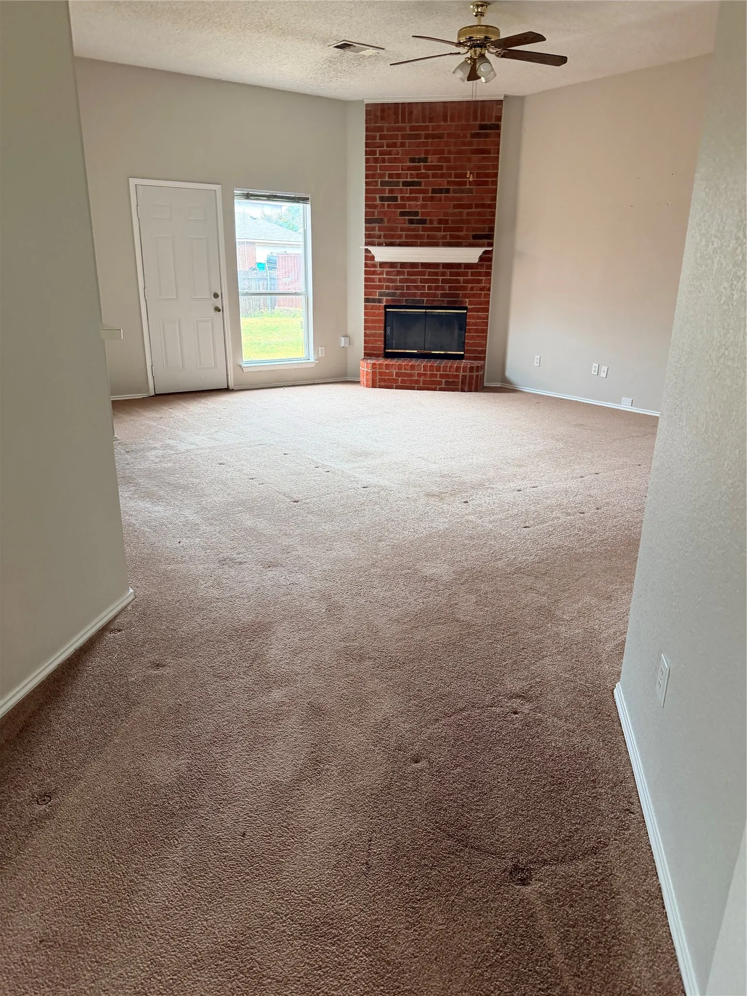 Vaulted ceiling with a ceiling fan, brick fireplace, and a large window