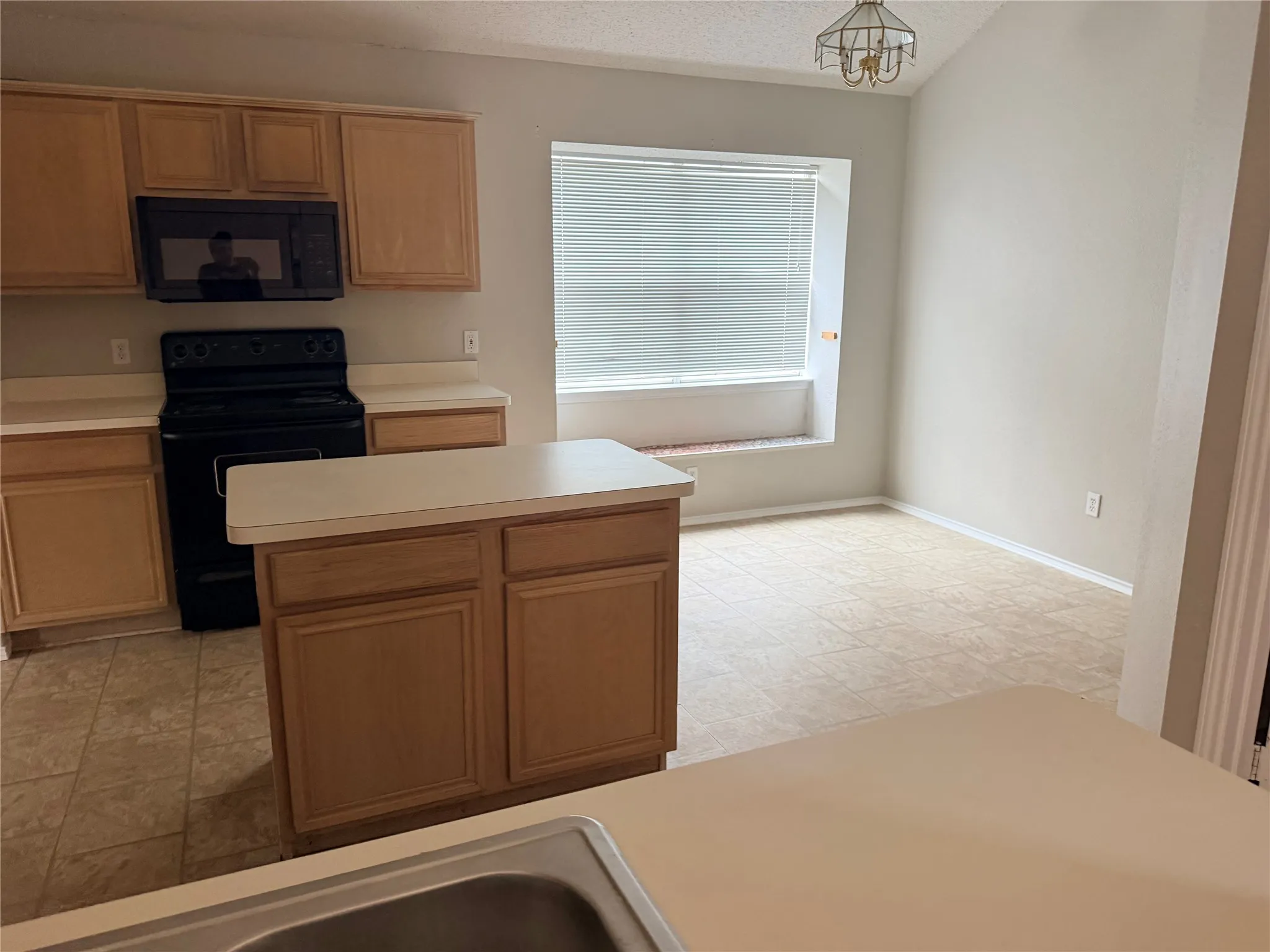 Kitchen featuring wood cabinetry, white countertops, black range, over-the-range microwave, and a central island