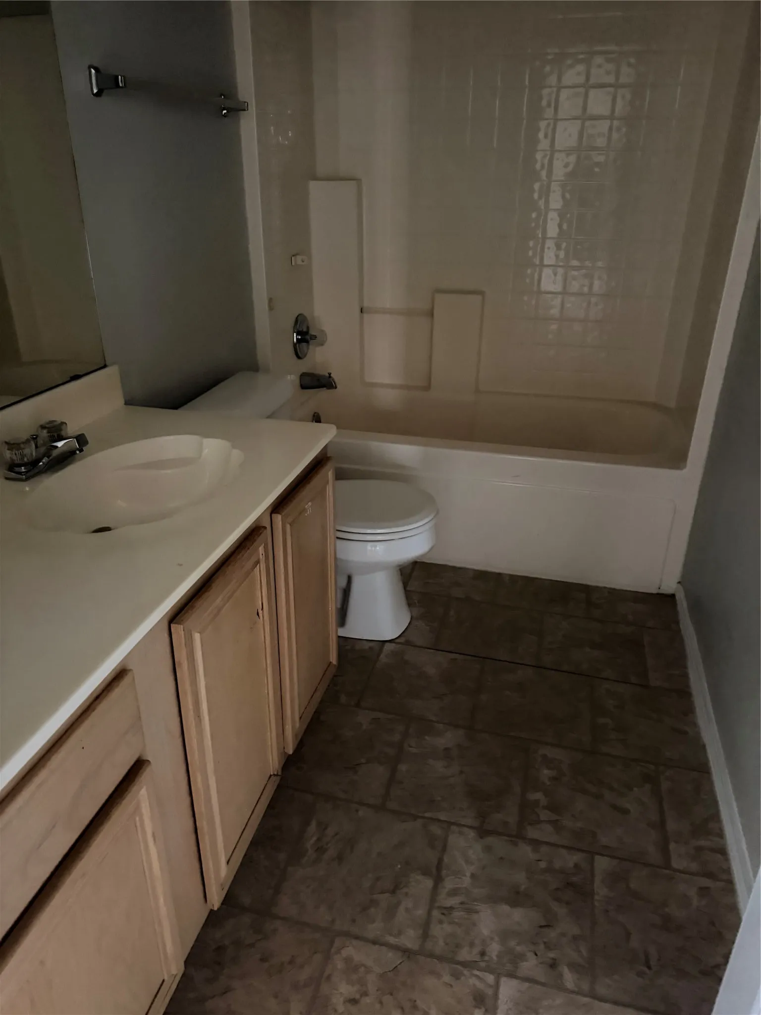 Tile flooring, wood-finish vanity with an integrated sink, and an enclosed bathtub with tile surround