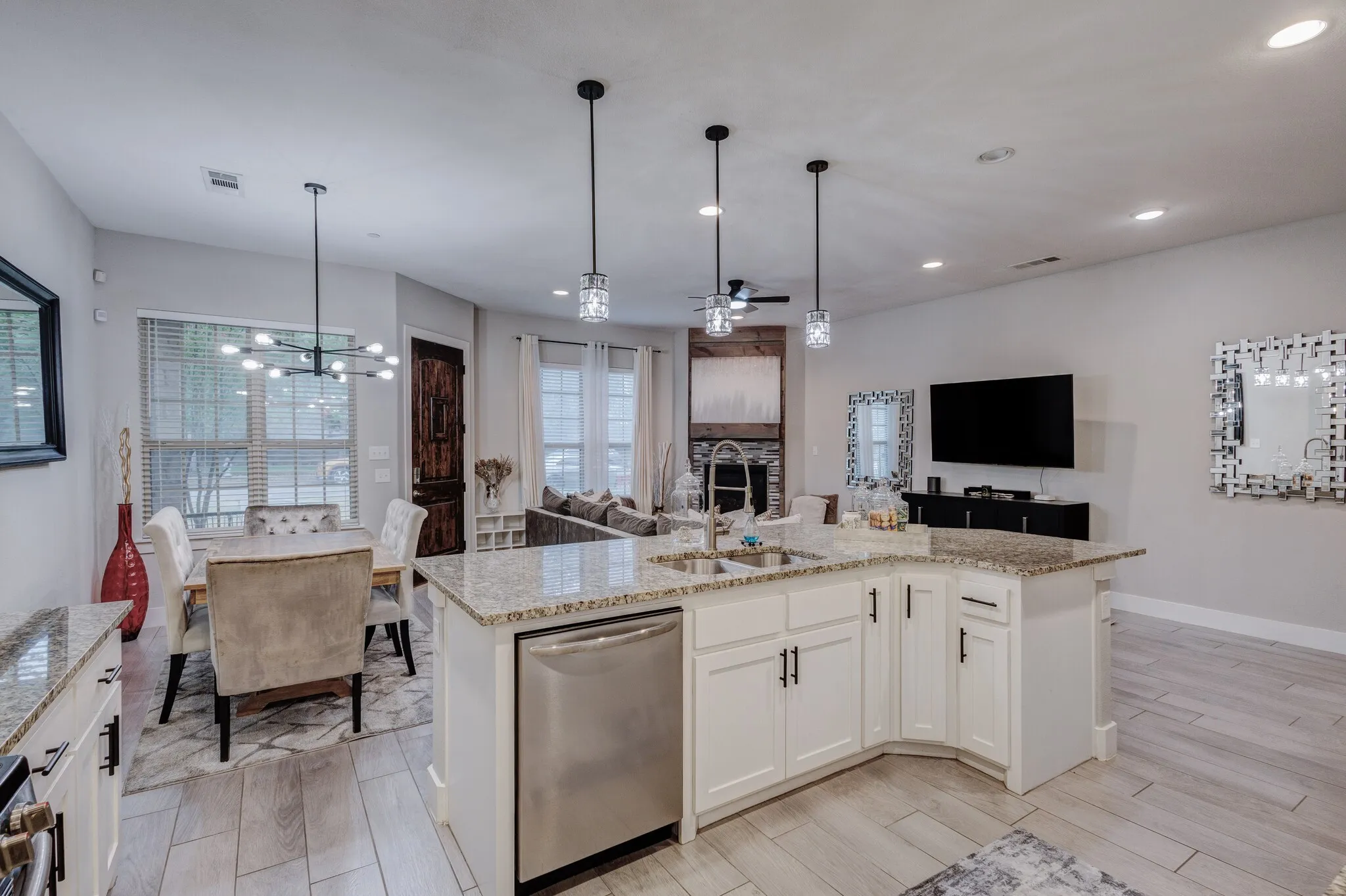 Kitchen island with white cabinetry and granite countertops, stainless steel dishwasher, pendant lighting fixtures, and light-toned wood-finish flooring