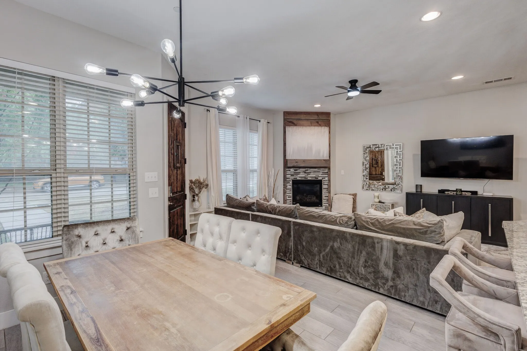 Open-concept living space with light wood-finish flooring, a contemporary chandelier, recessed lighting, and a built-in fireplace with a stone surround and wood mantle
