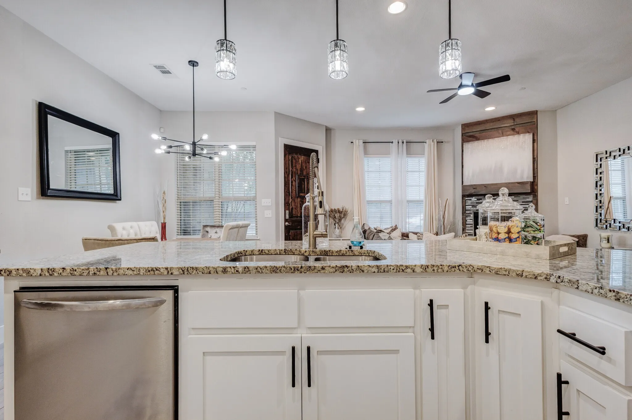 Kitchen island featuring a stainless steel sink with a high-arch faucet, granite-style countertop, and white cabinetry with matte black hardware