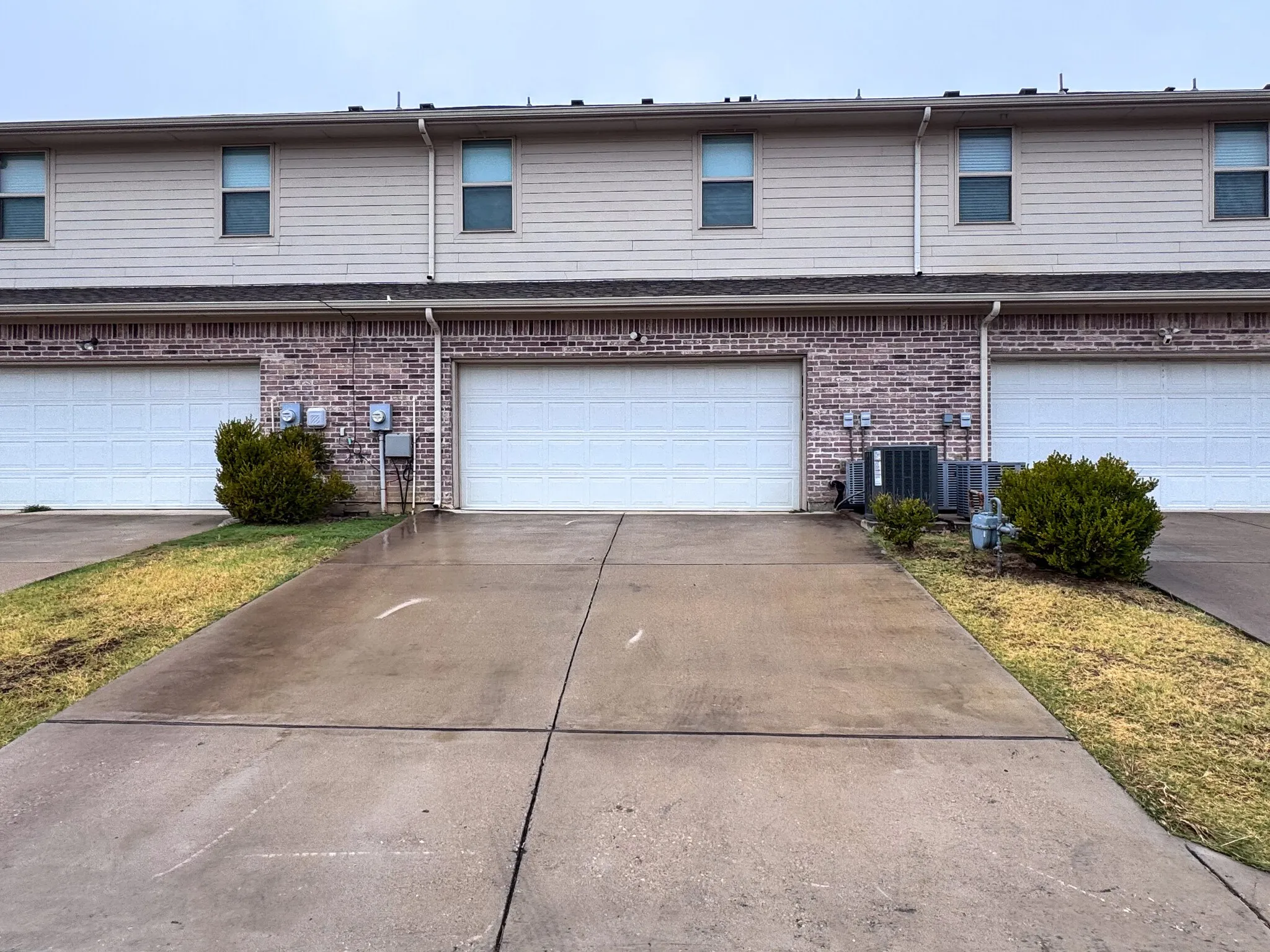 Brick and siding exterior featuring white garage doors, upper-level windows, and concrete driveways