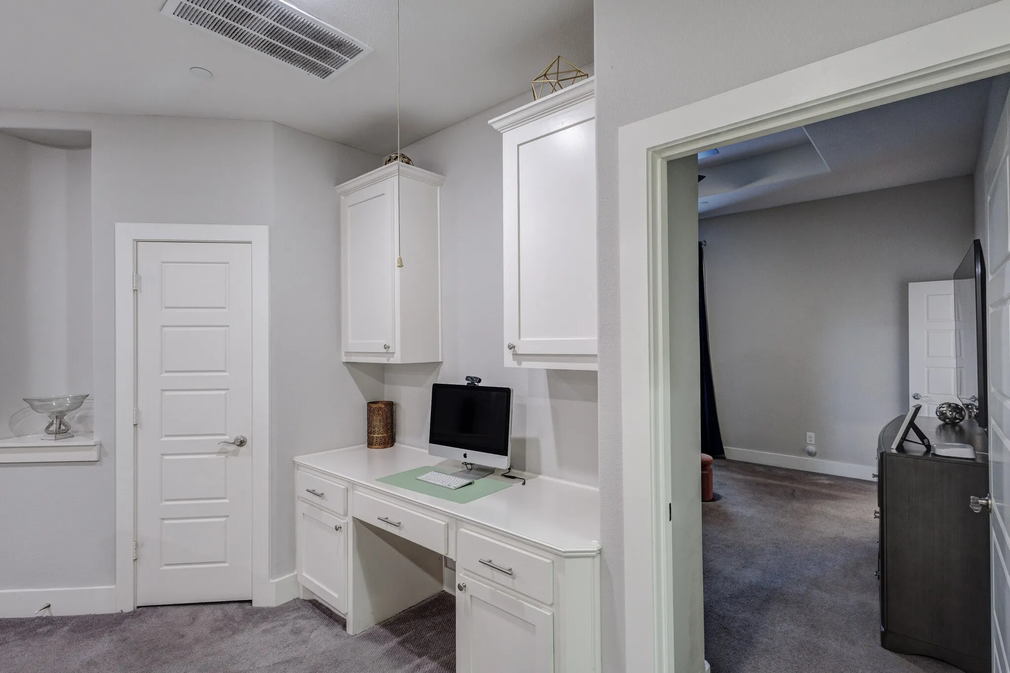 Built-in desk with white cabinetry and chrome hardware, white paneled doors, and grey carpeting