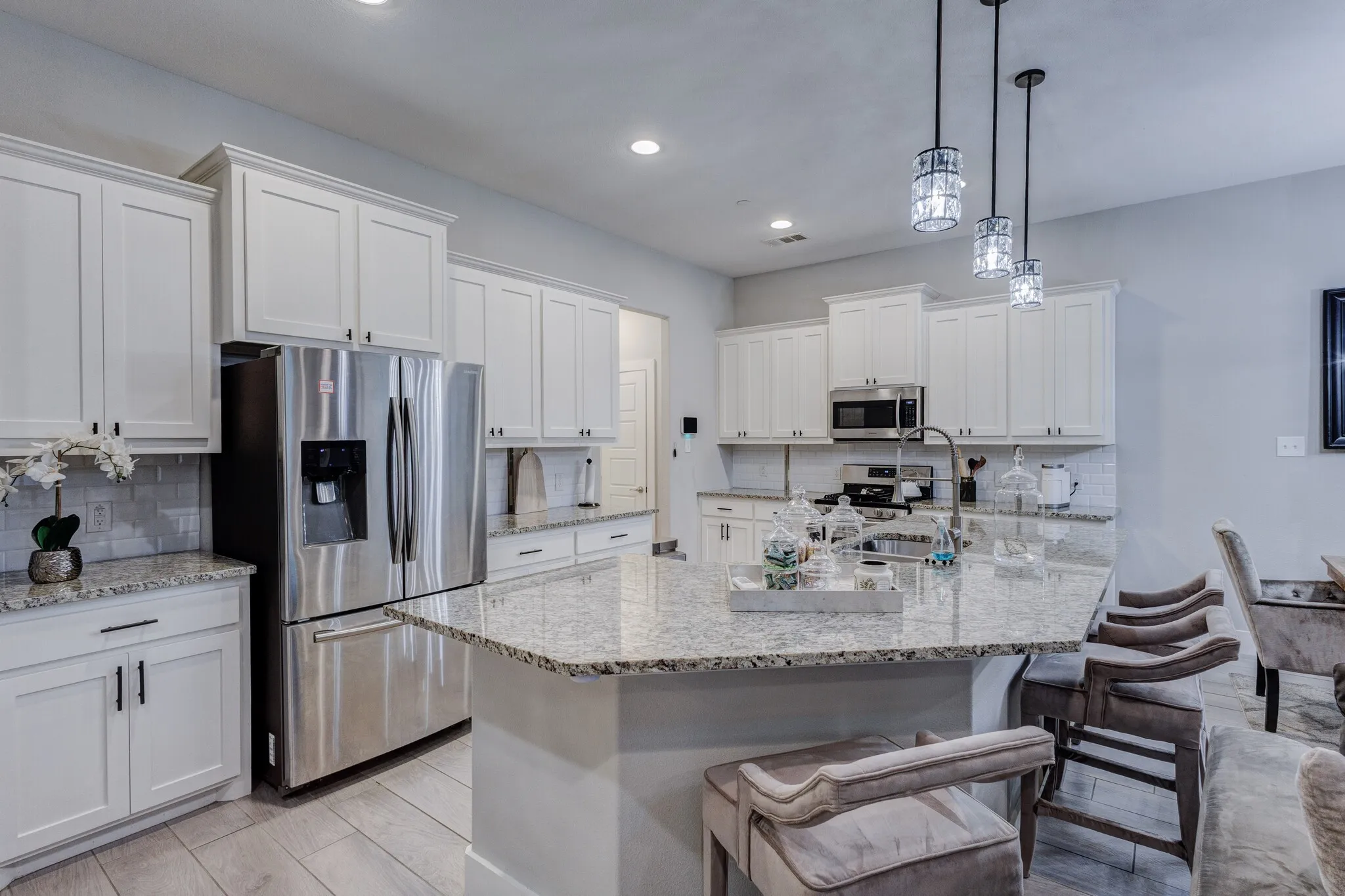 White shaker cabinetry, stainless steel appliances, speckled stone countertops, tile backsplash, and decorative pendant lighting