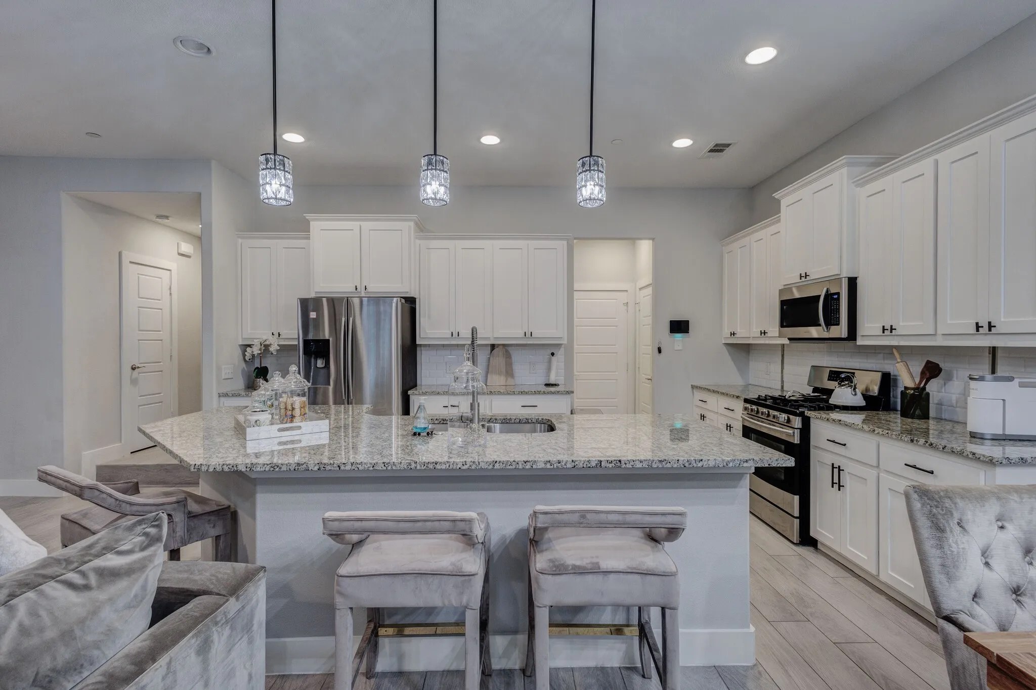 Kitchen featuring a large island with stone countertop, white shaker cabinetry, stainless steel appliances, and pendant lighting