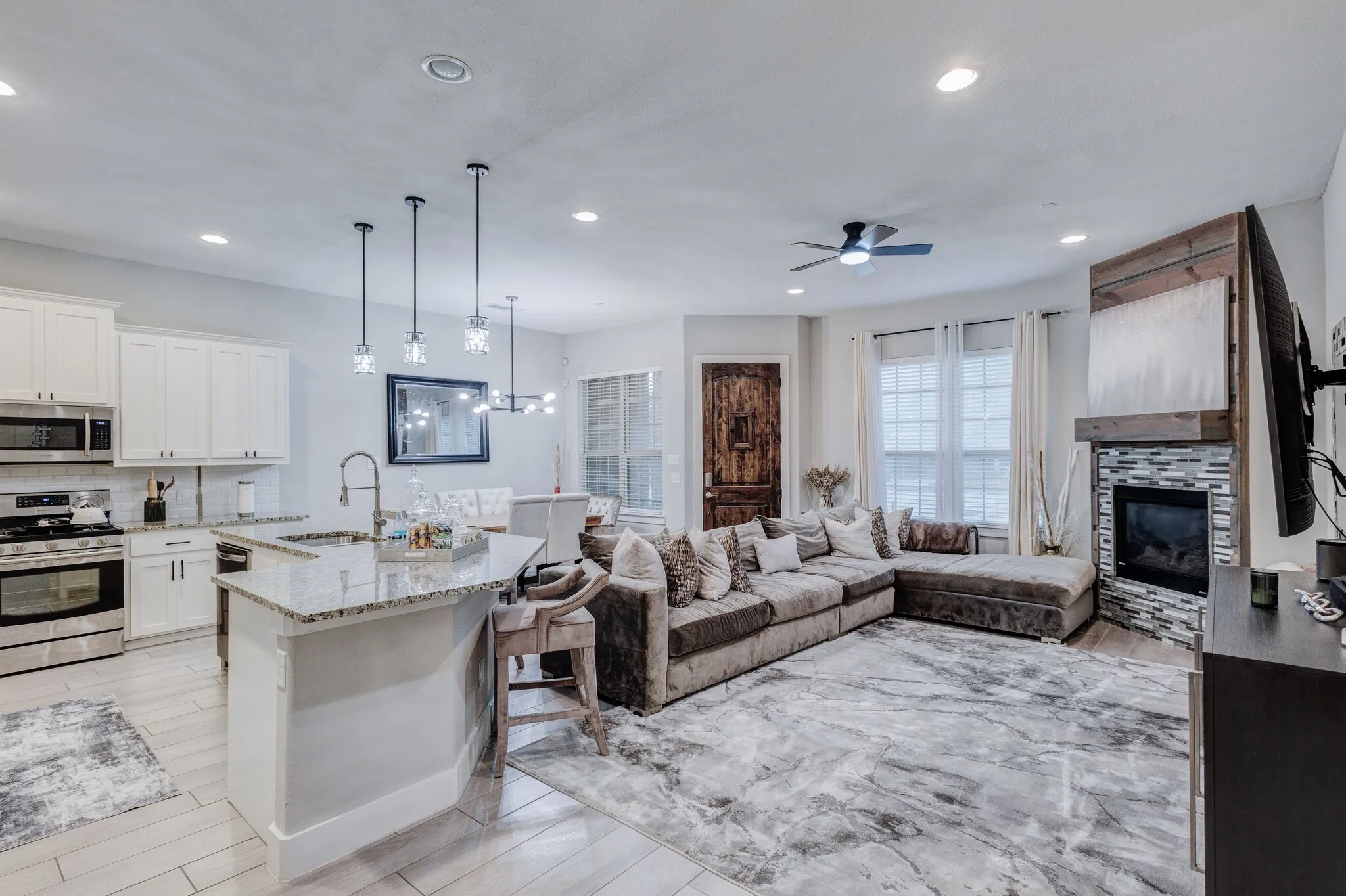 Open-concept living area featuring wood-finish flooring, a kitchen island with stone countertop, stainless steel appliances, and a tiled fireplace
