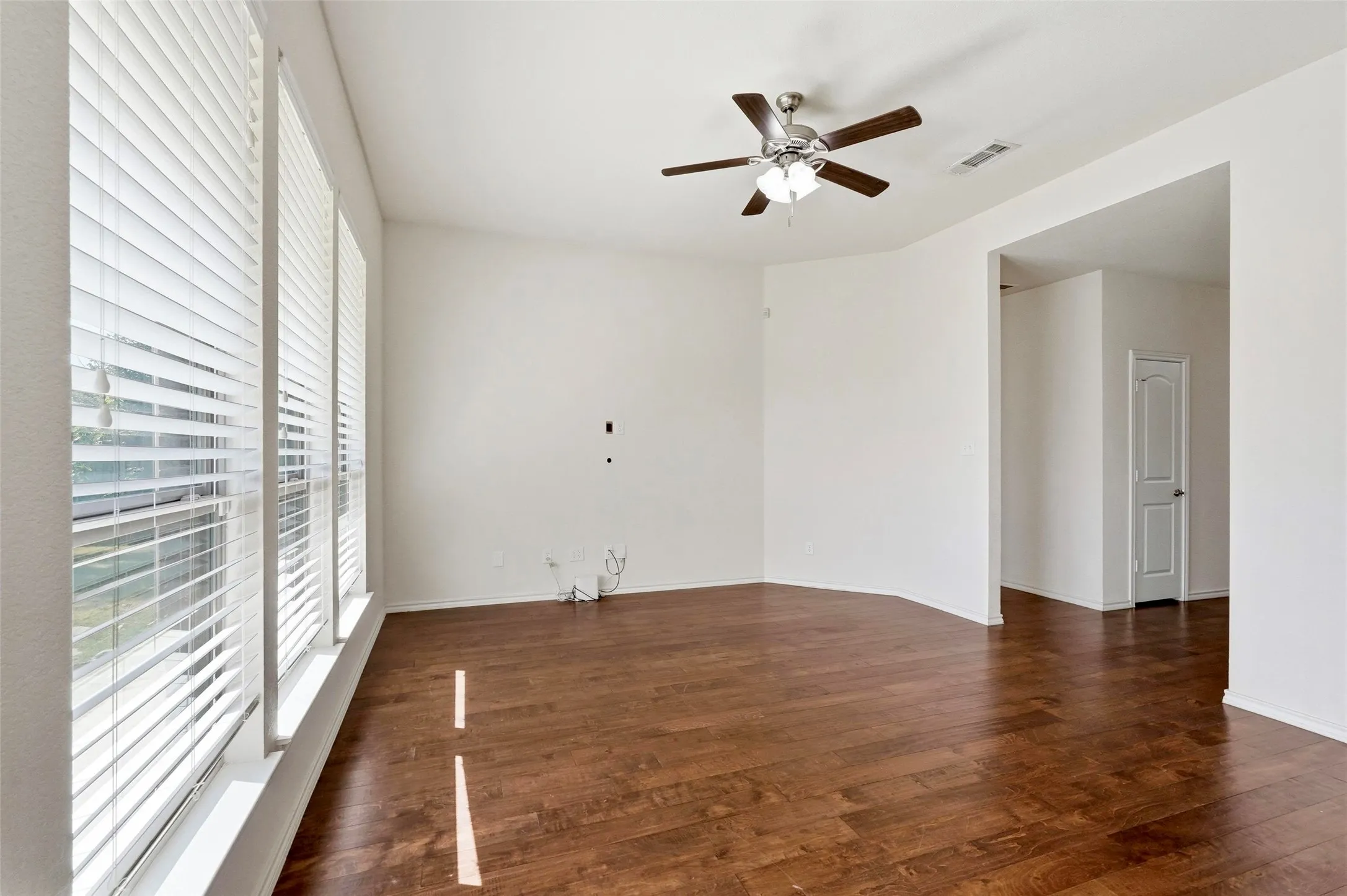 Wood-finish flooring throughout, multiple windows with blinds, ceiling fan with integrated lighting, and an arched doorway